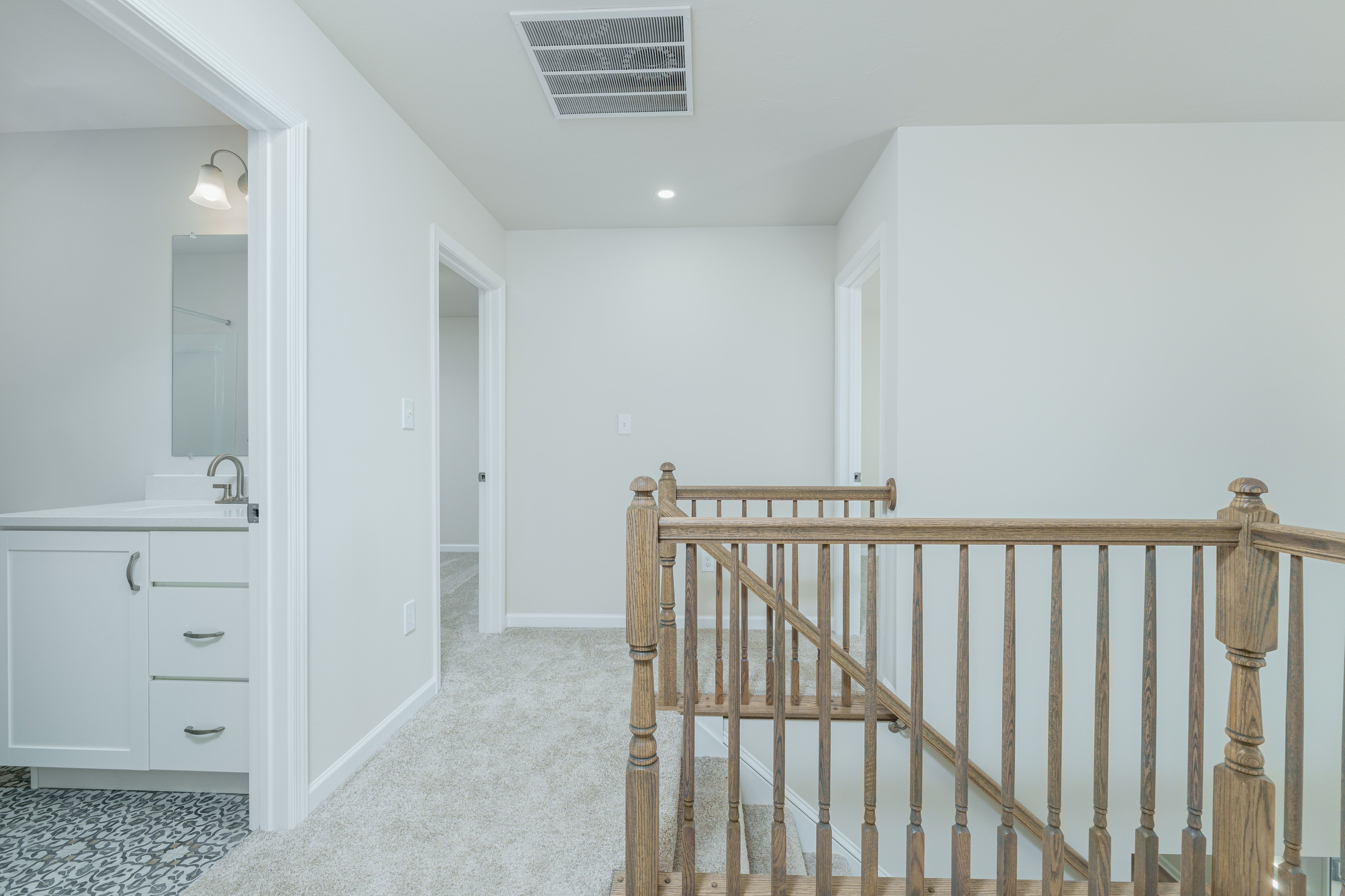 Upstairs landing with wood railing, carpet flooring, and hallway leading to bedrooms and bath.
