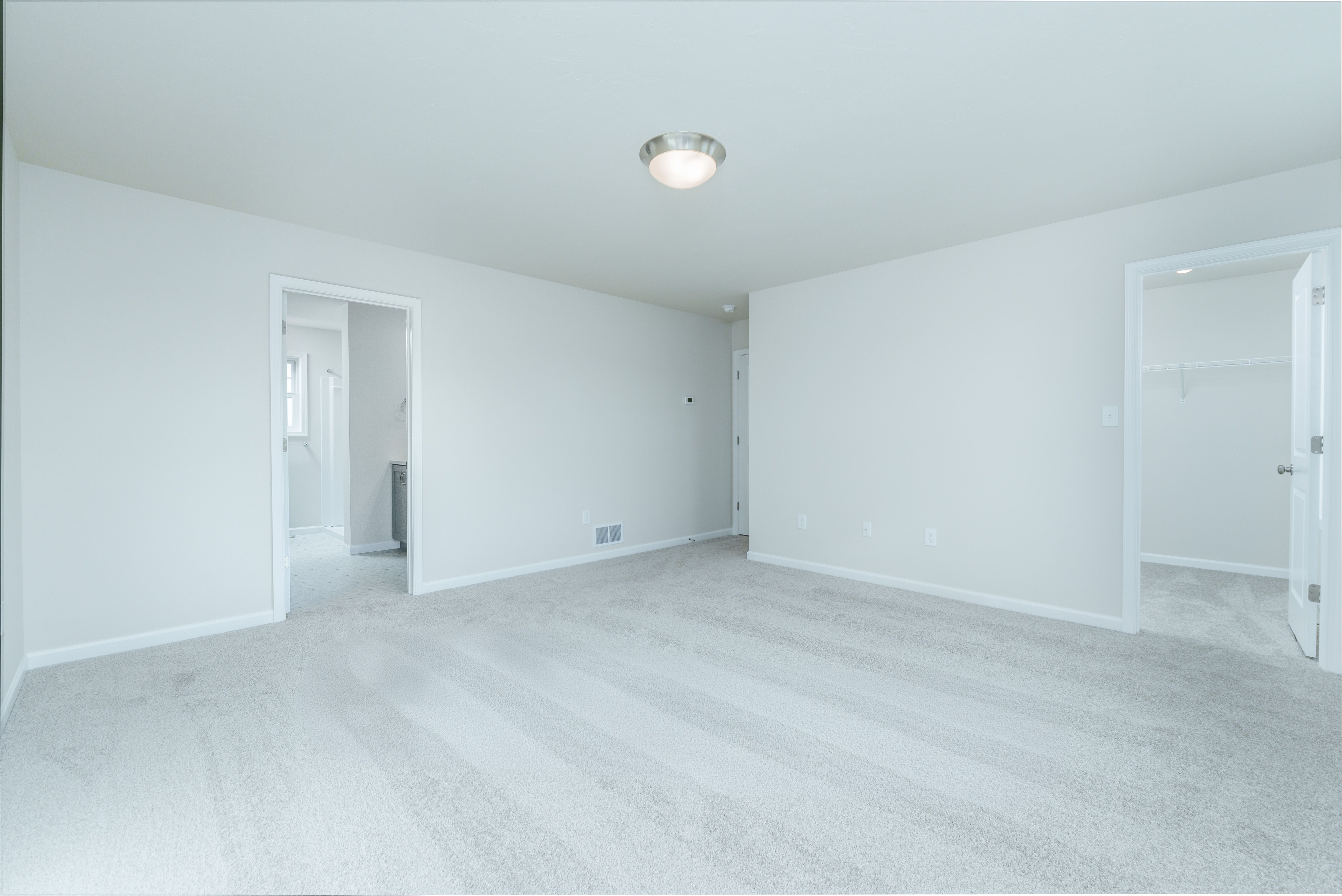 Owners bedroom with plush carpet, single window, and doorway leading to walk-in closet.