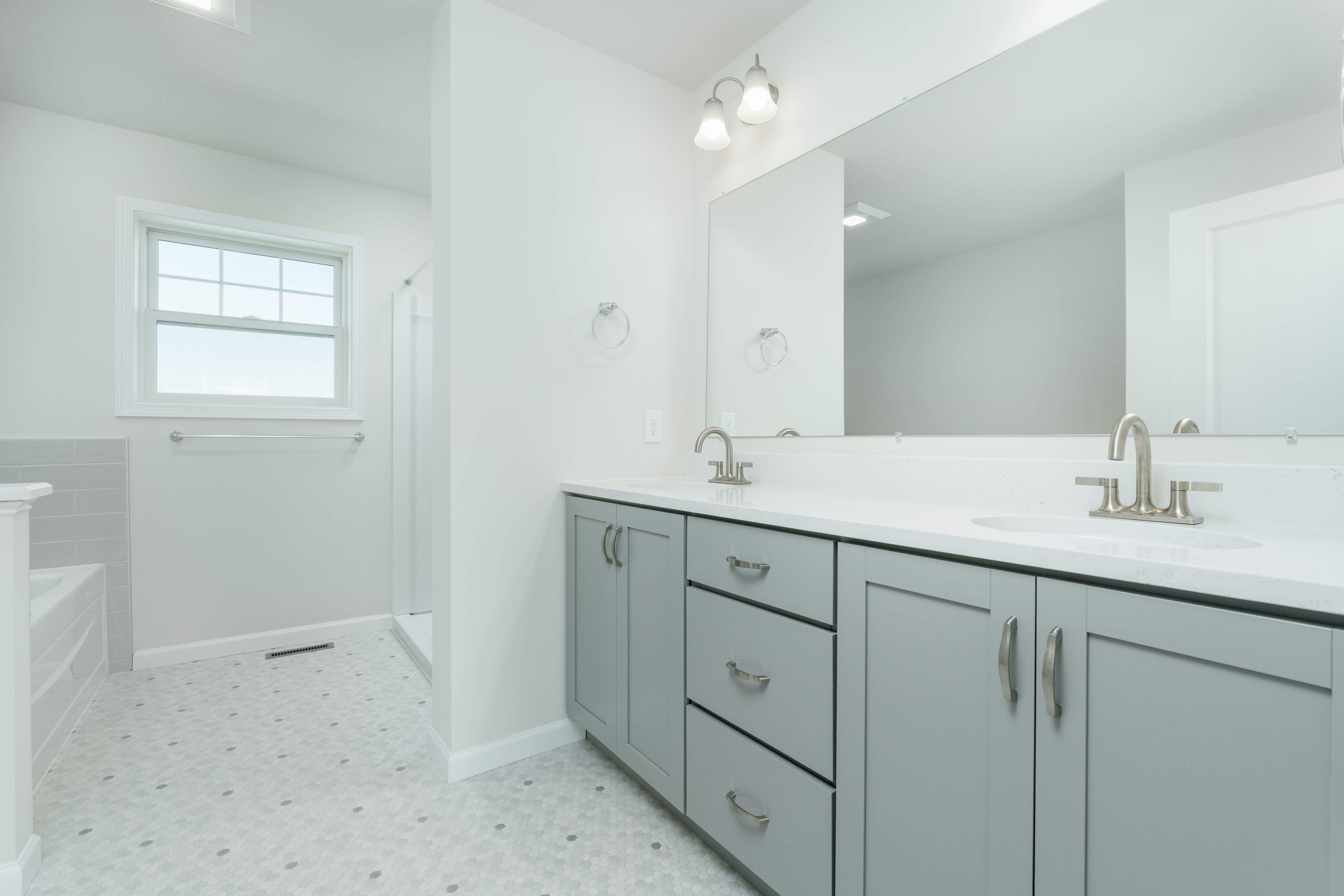 Owners bath with double sink gray vanity, quartz countertop, large mirror, and hex tile flooring.