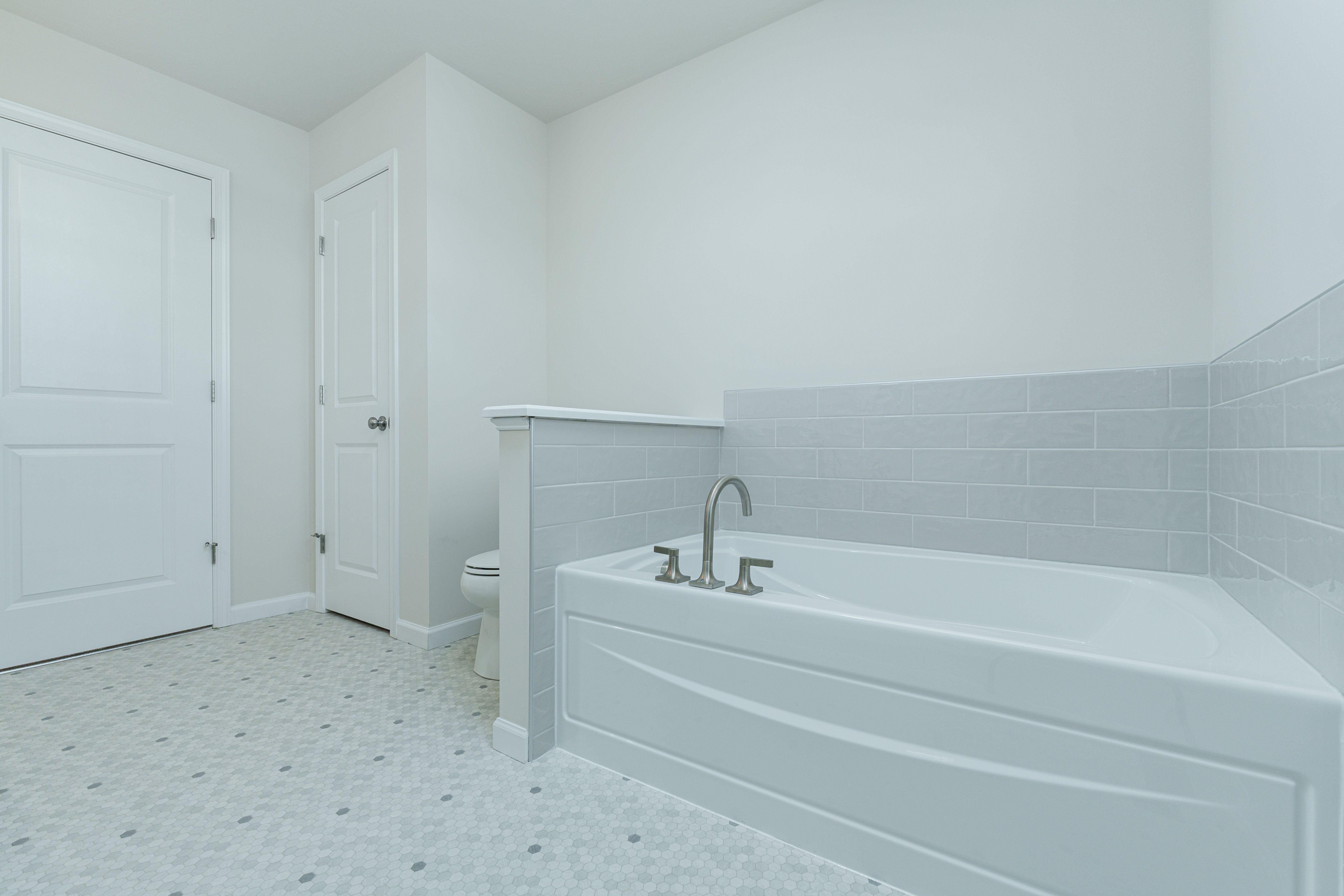 Owners bathroom with soaking tub, brushed nickel faucet, subway tile surround, and hex tile flooring.