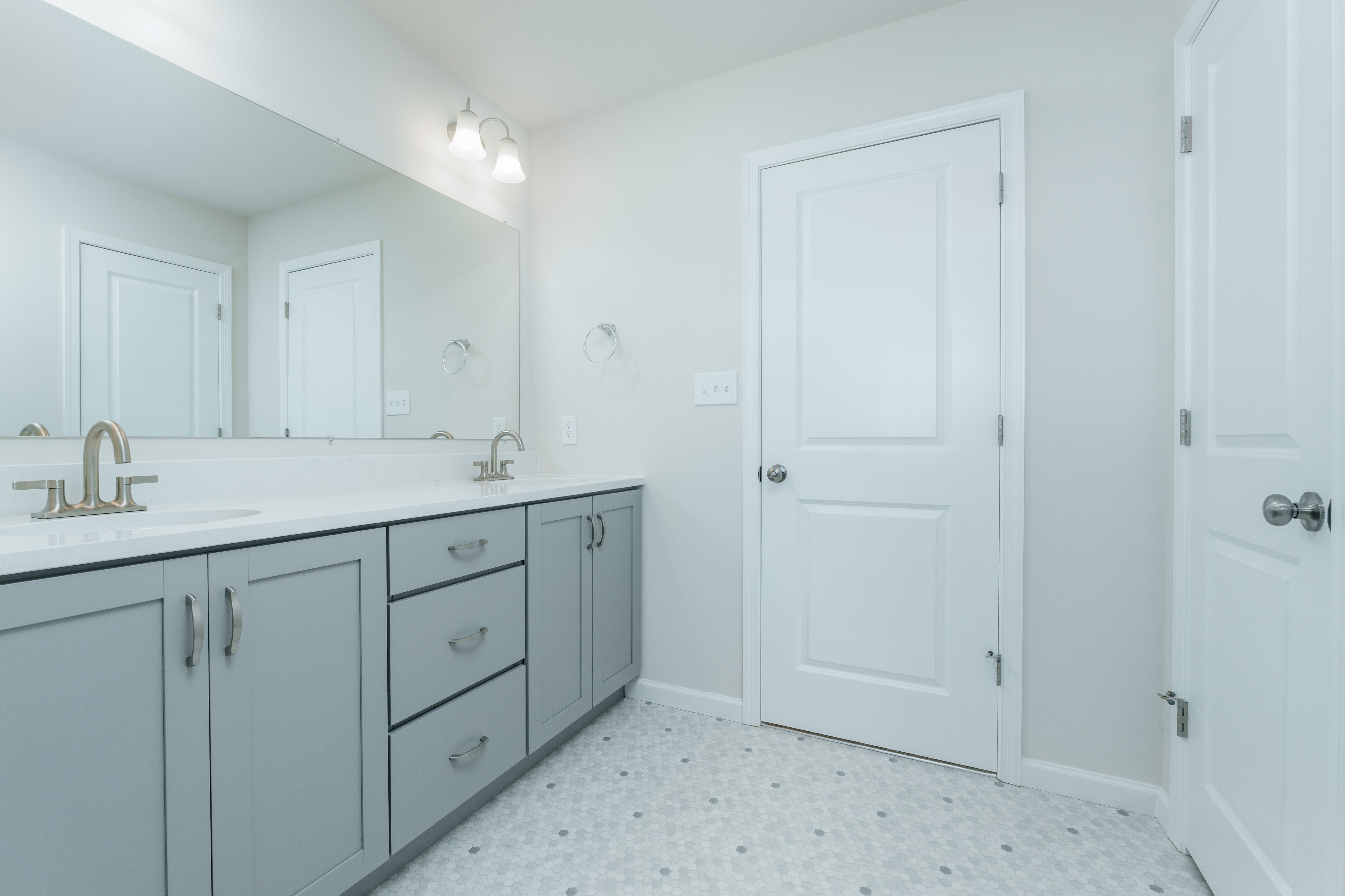 Owners bath featuring double vanity with gray cabinets, quartz countertop, and wide wall mirror.