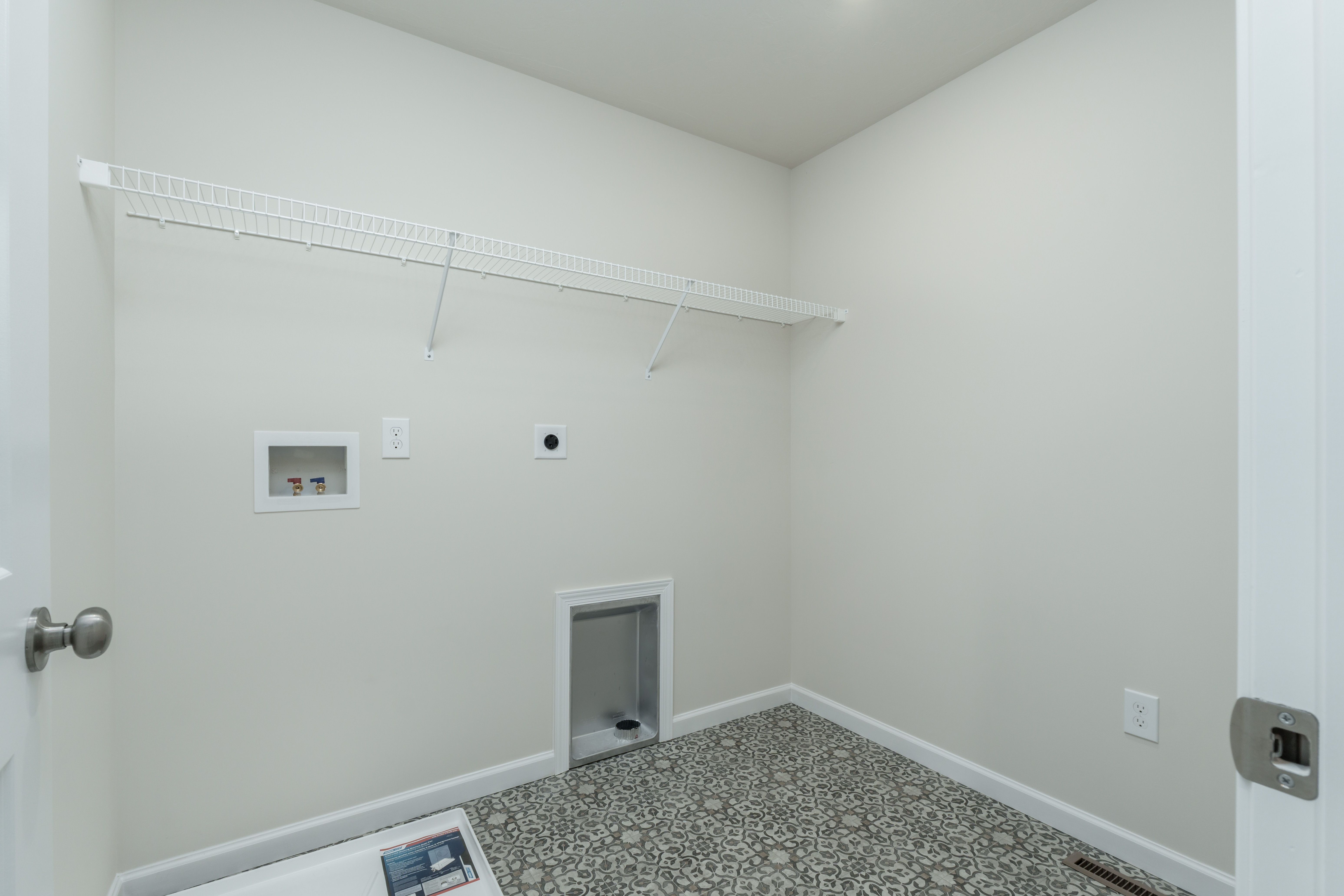 Laundry room with wire shelf, washer and dryer hookups, utility sink drain, and patterned tile flooring.