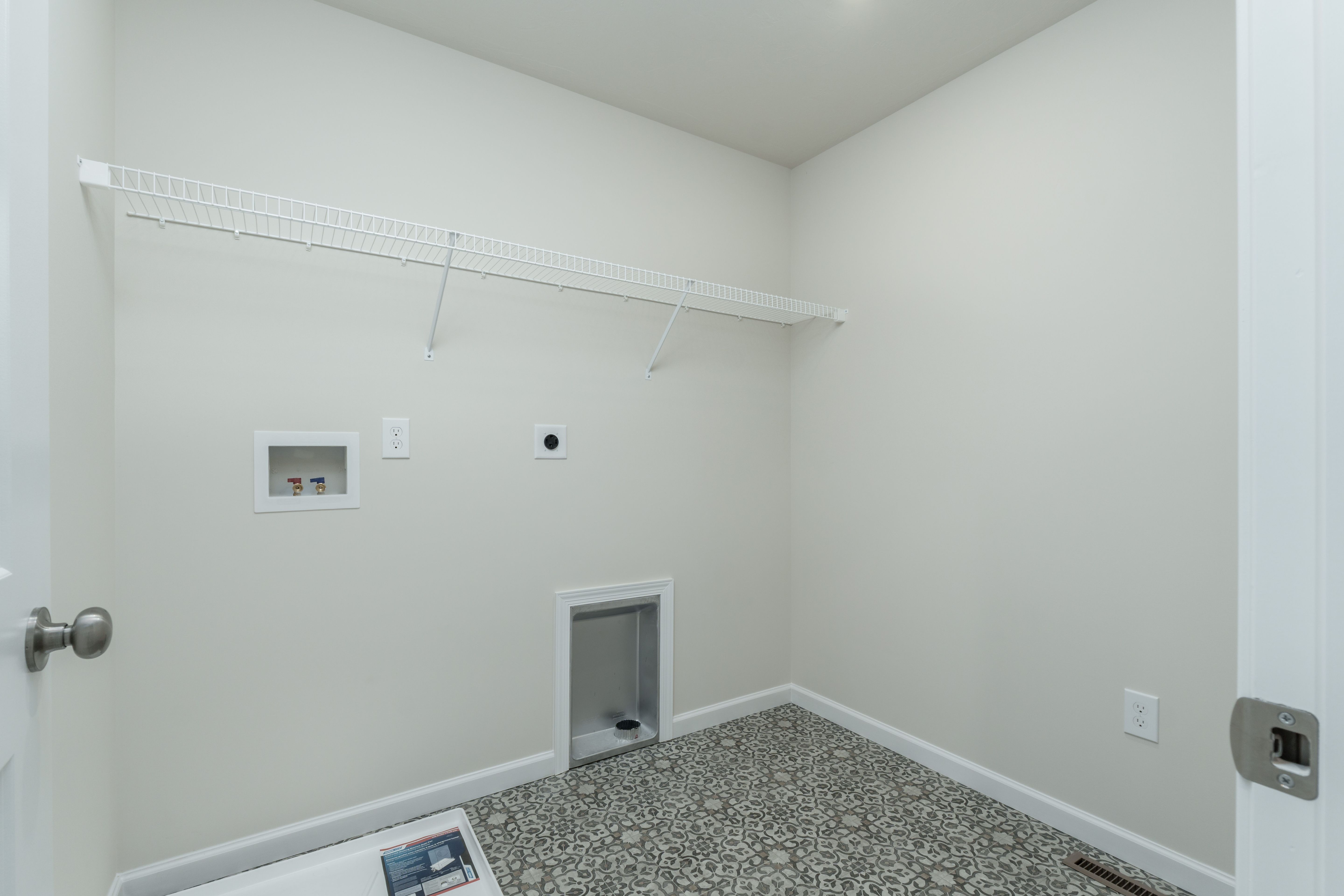 Laundry room with wire shelf, washer and dryer hookups, utility sink drain, and patterned tile flooring.