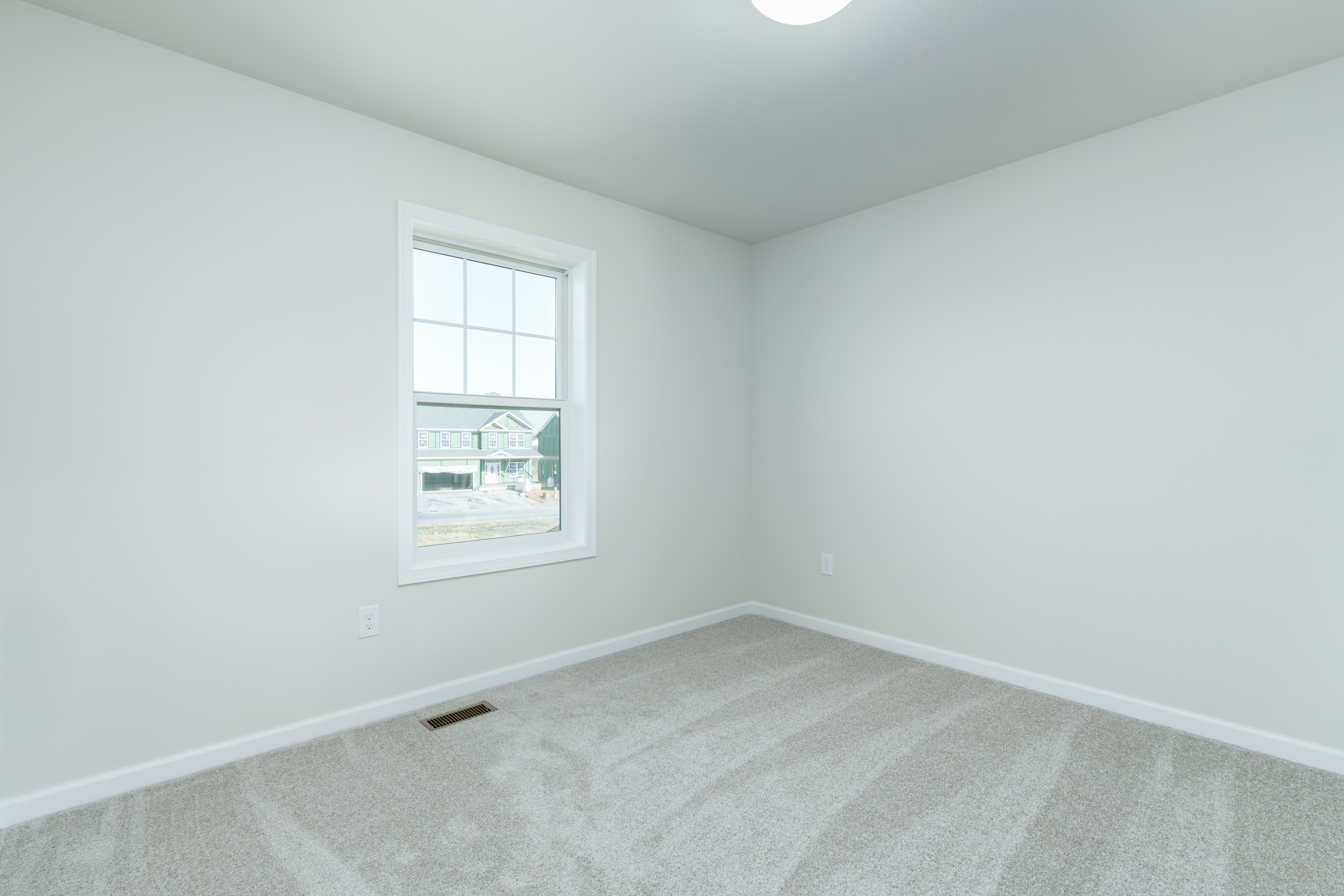 Bedroom with light carpet, single window, white walls, and simple ceiling light fixture.