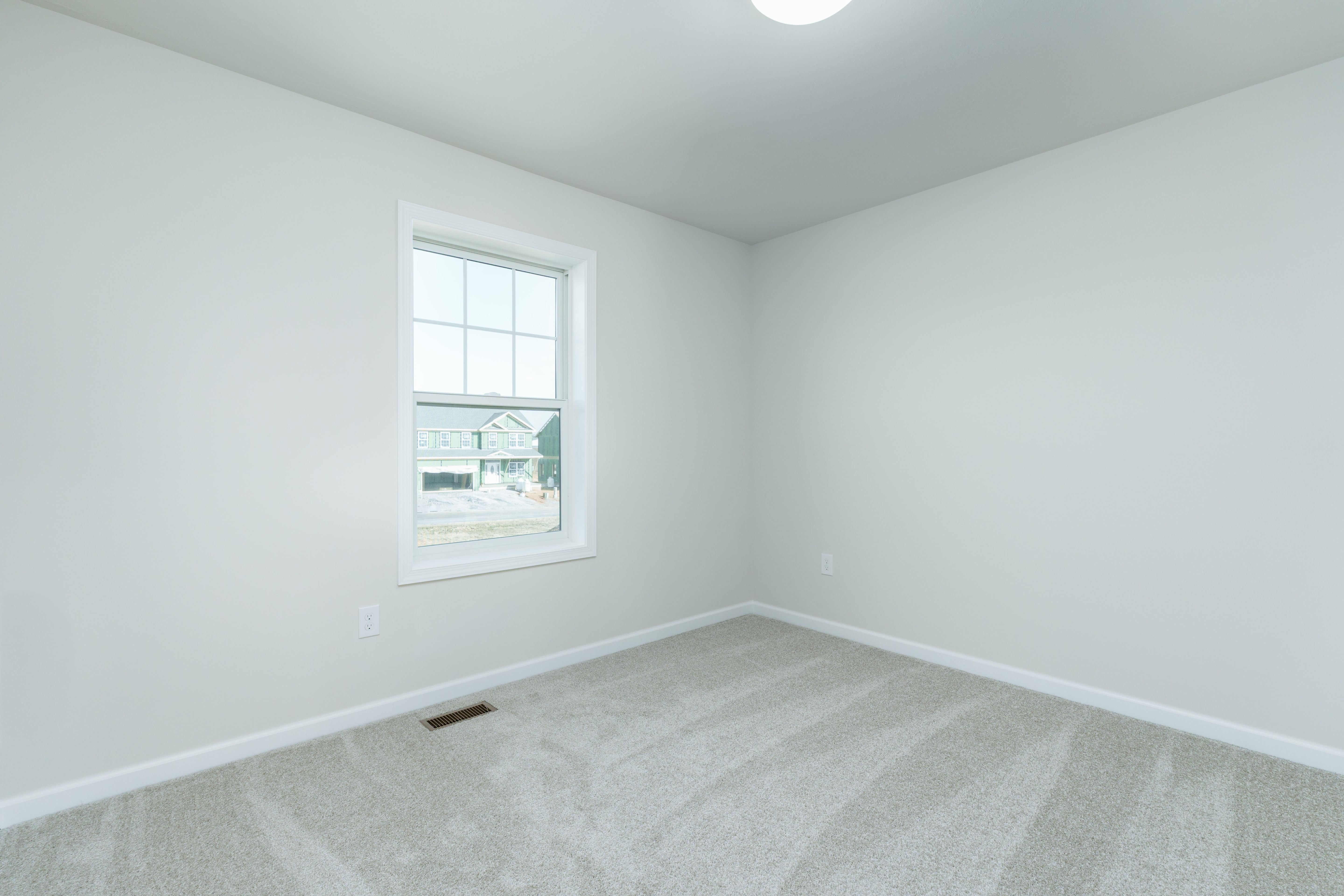 Bedroom with light carpet, single window, white walls, and simple ceiling light fixture.