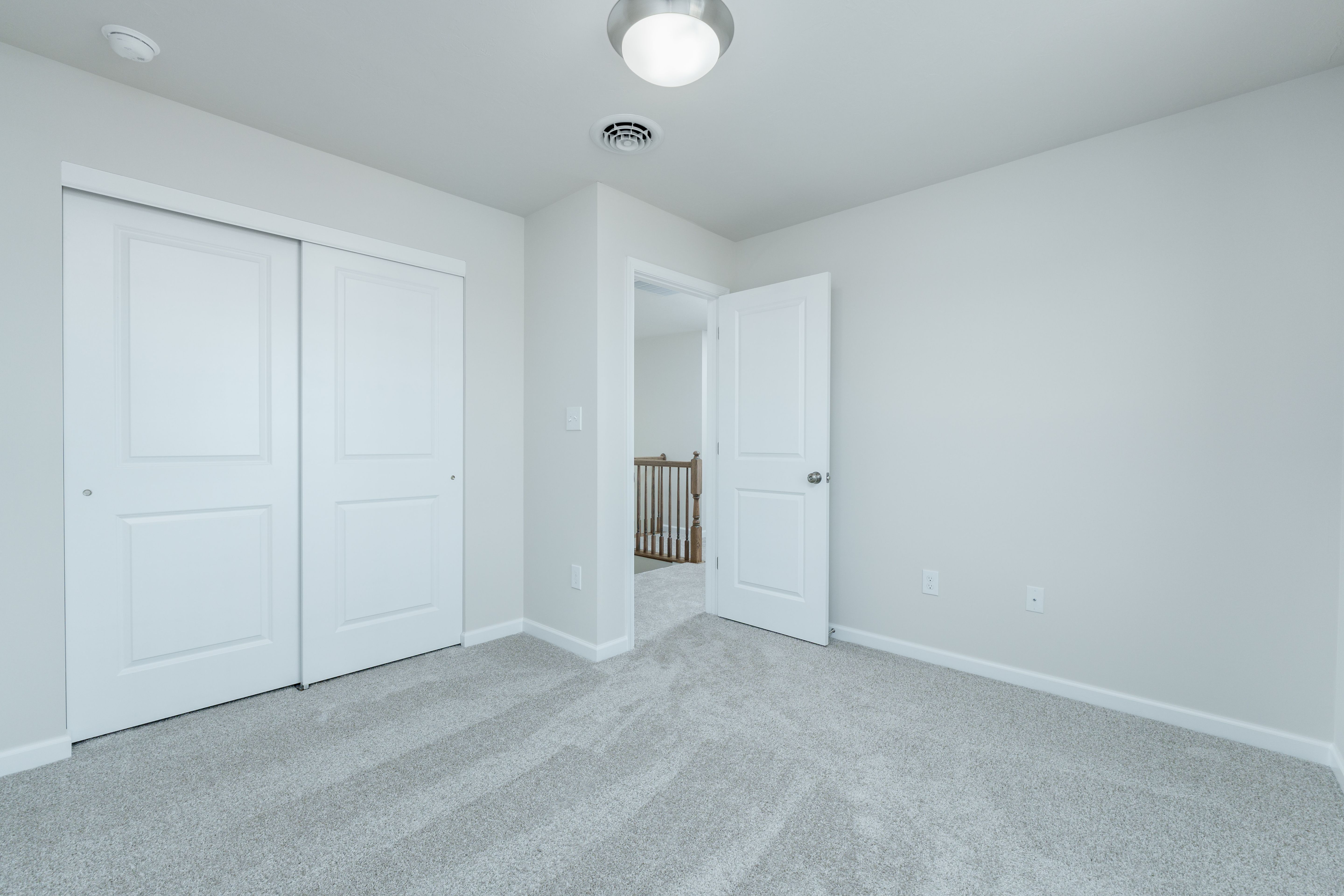 Bedroom with carpet, sliding closet doors, white trim, and open door leading to hallway railing.