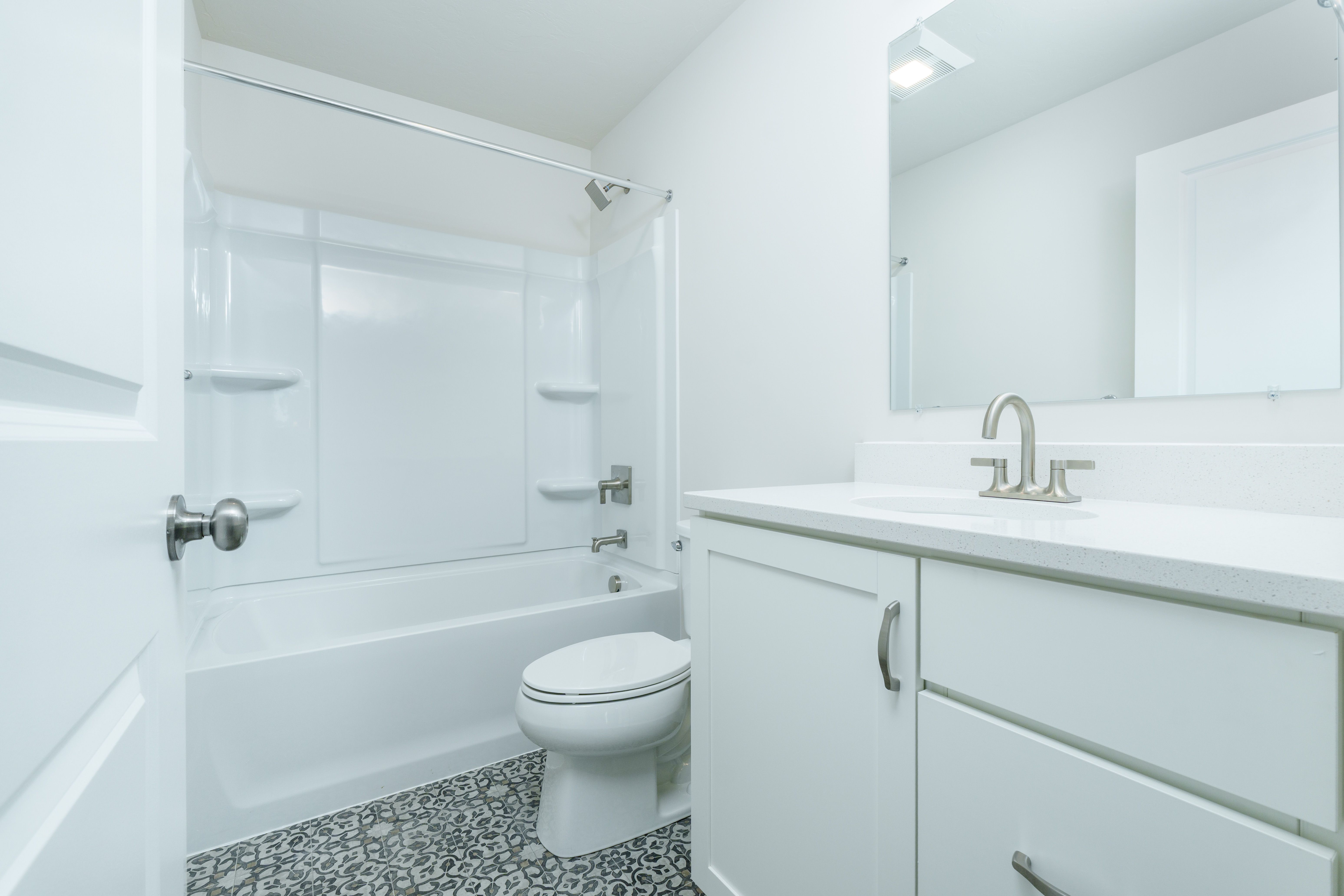 Full bathroom with white tub and shower surround, single sink vanity, brushed nickel fixtures, and patterned tile flooring.