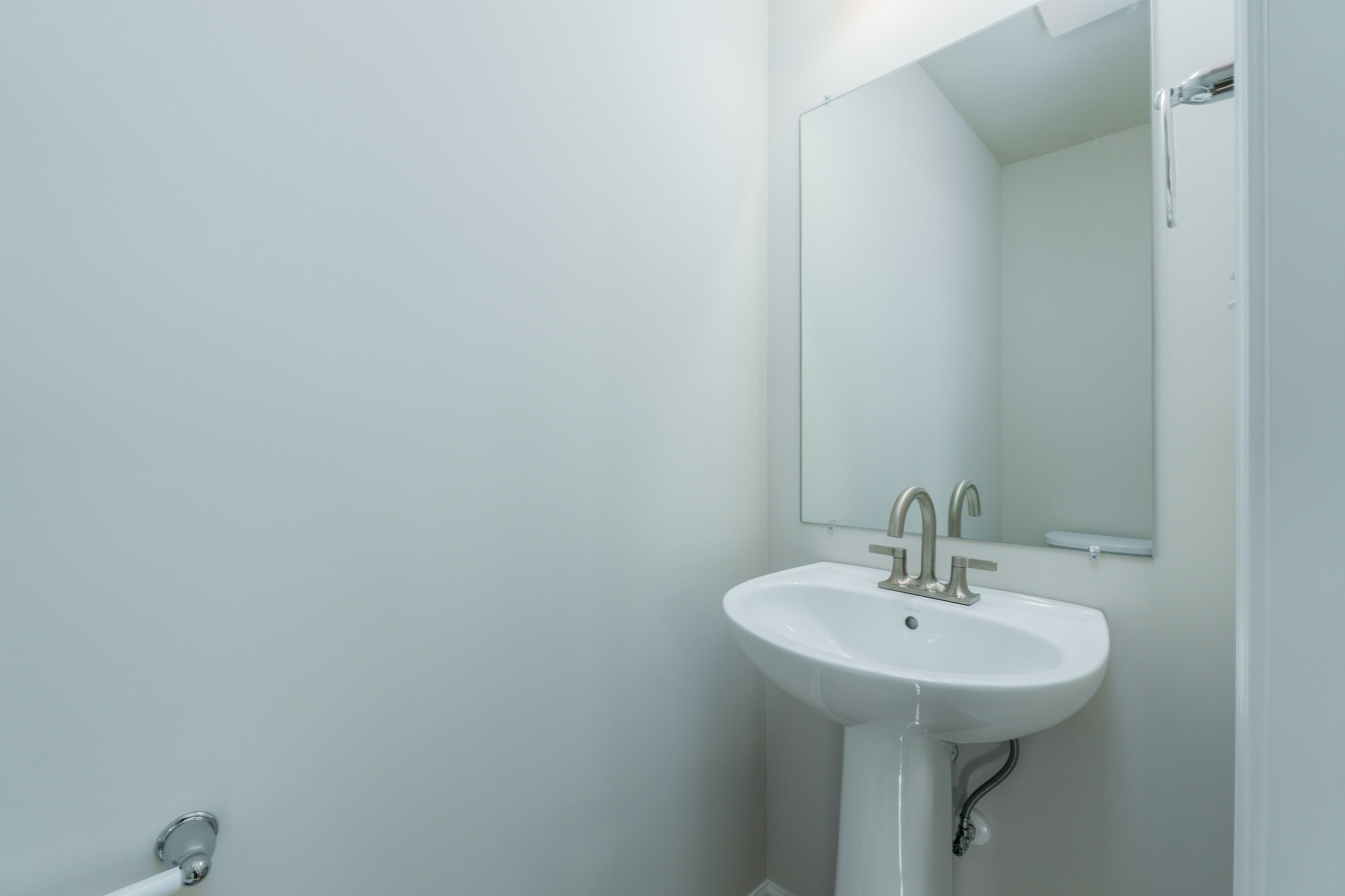 Powder room with pedestal sink, brushed nickel faucet, wall mirror, and neutral walls.
