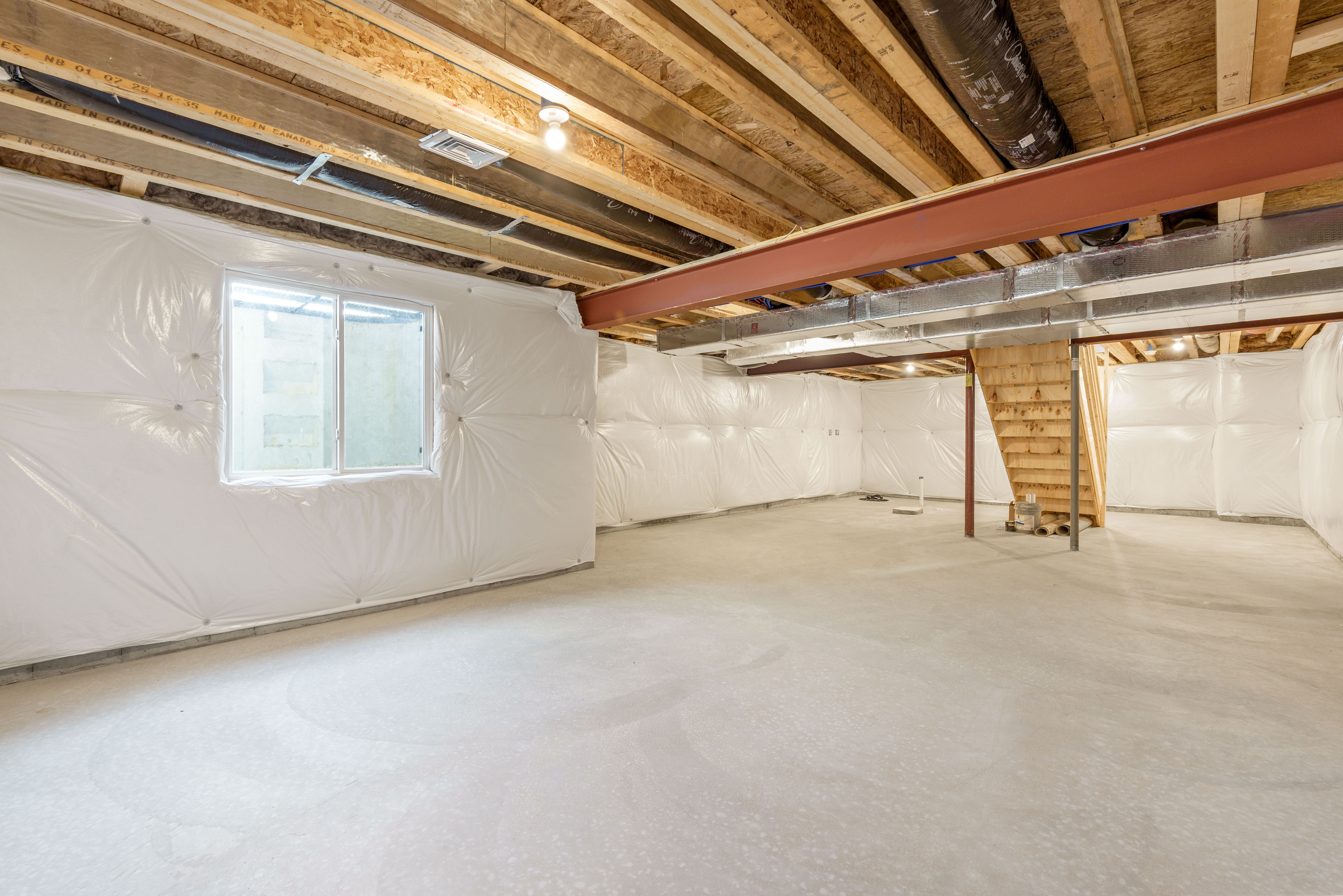 Unfinished basement with egress window, steel beam, wood staircase, and insulated walls over concrete floors.
