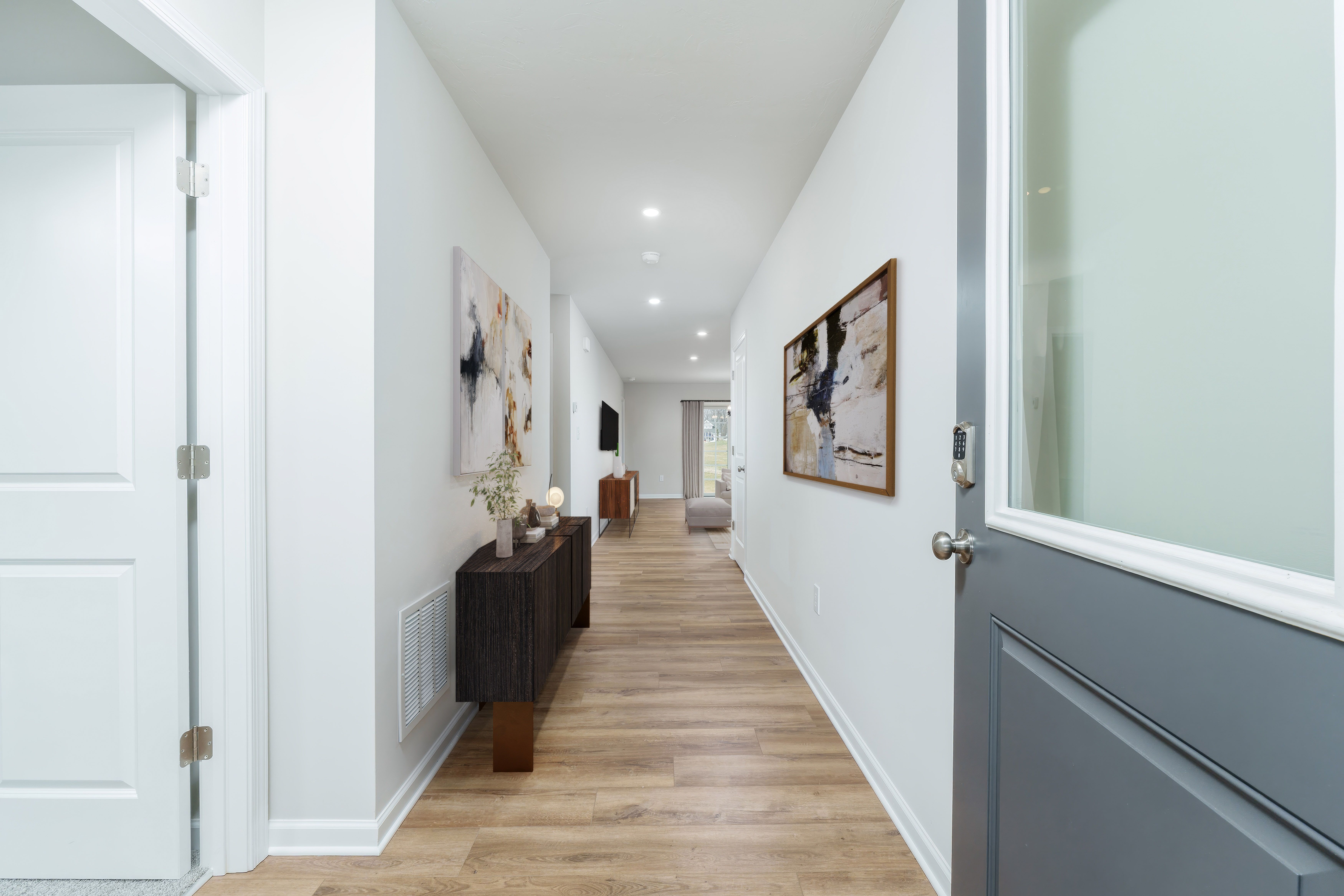 Long foyer hallway with luxury vinyl plank flooring, modern console table, wall art, and view toward living area.