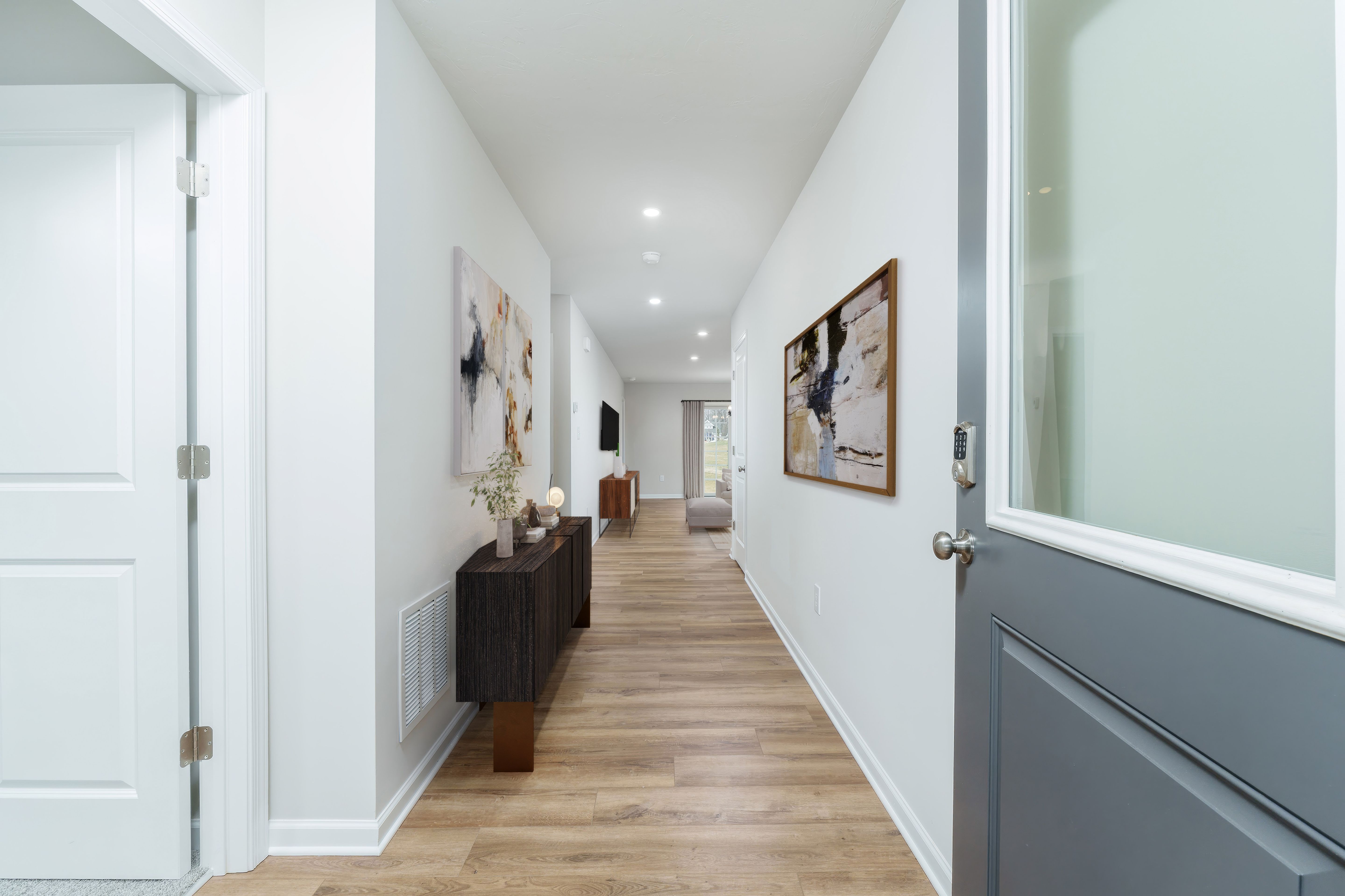 Long foyer hallway with luxury vinyl plank flooring, modern console table, wall art, and view toward living area.