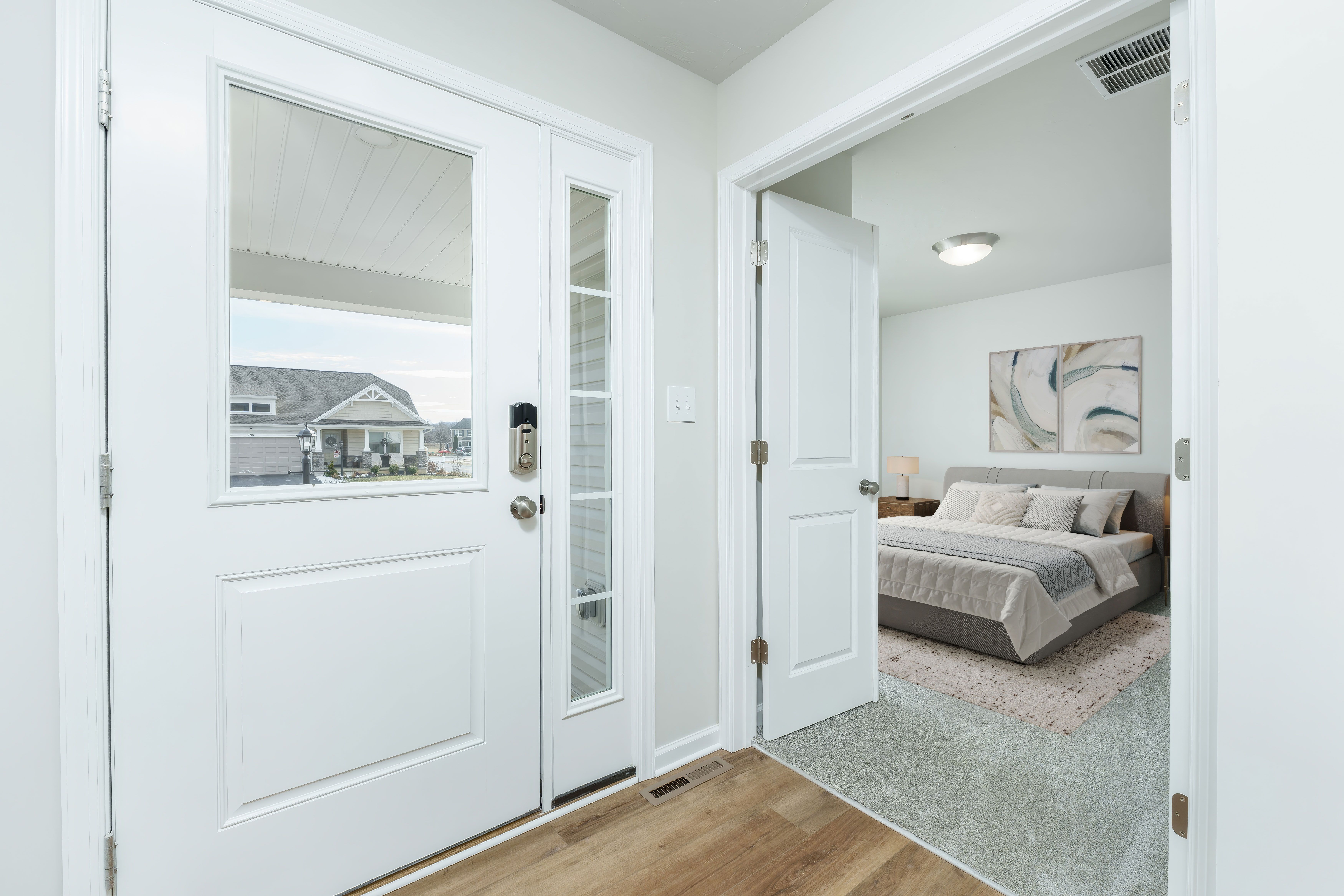 Front entry with glass panel door, luxury vinyl plank flooring, and view into adjacent bedroom.