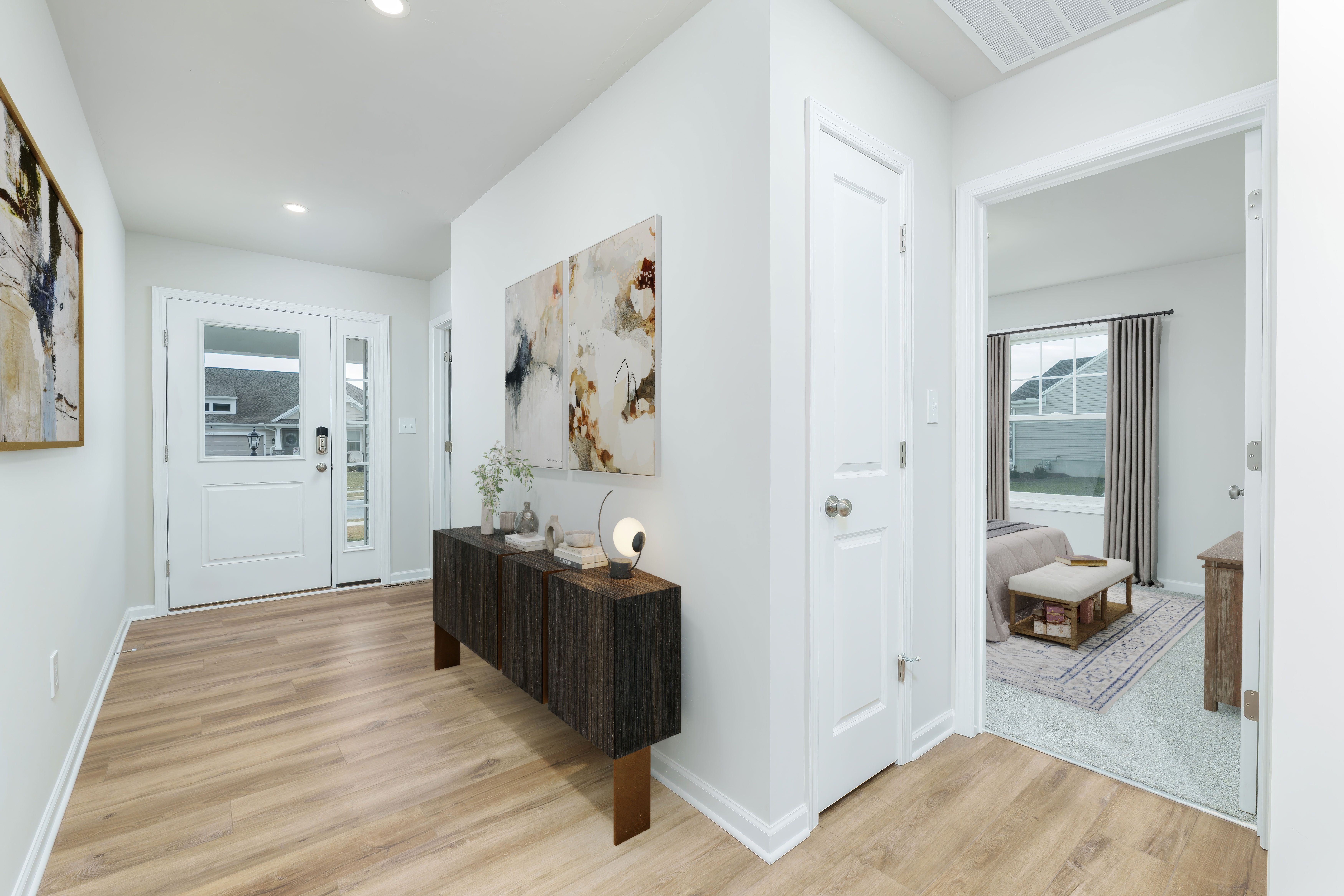 Entry hallway with luxury vinyl plank flooring, decorative console table, abstract art, and bedroom doorway.