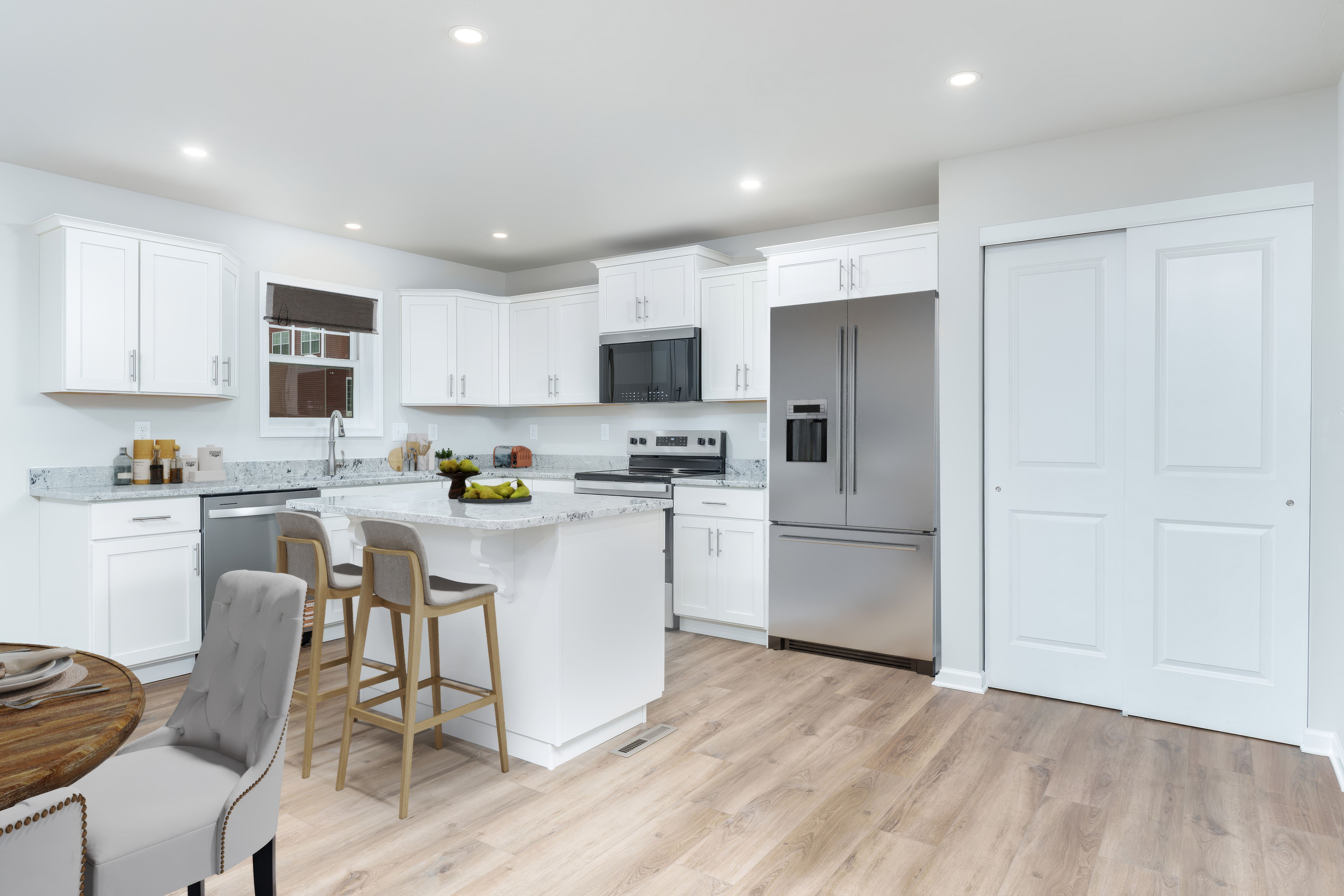 Spacious kitchen with center island, stainless refrigerator, white cabinets, and luxury vinyl plank flooring.