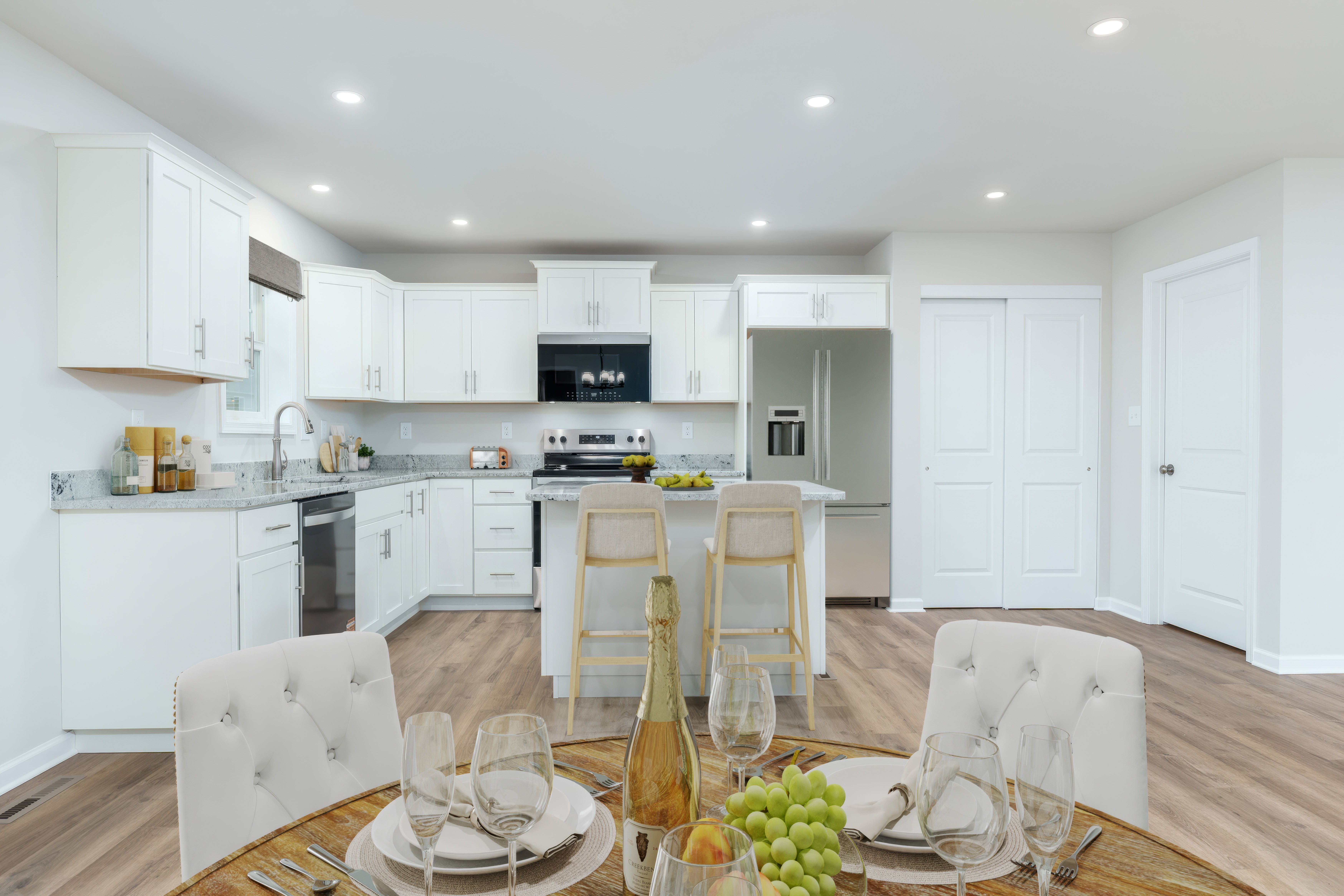 Open kitchen with large island seating, white cabinets, stainless appliances, and luxury vinyl plank flooring.