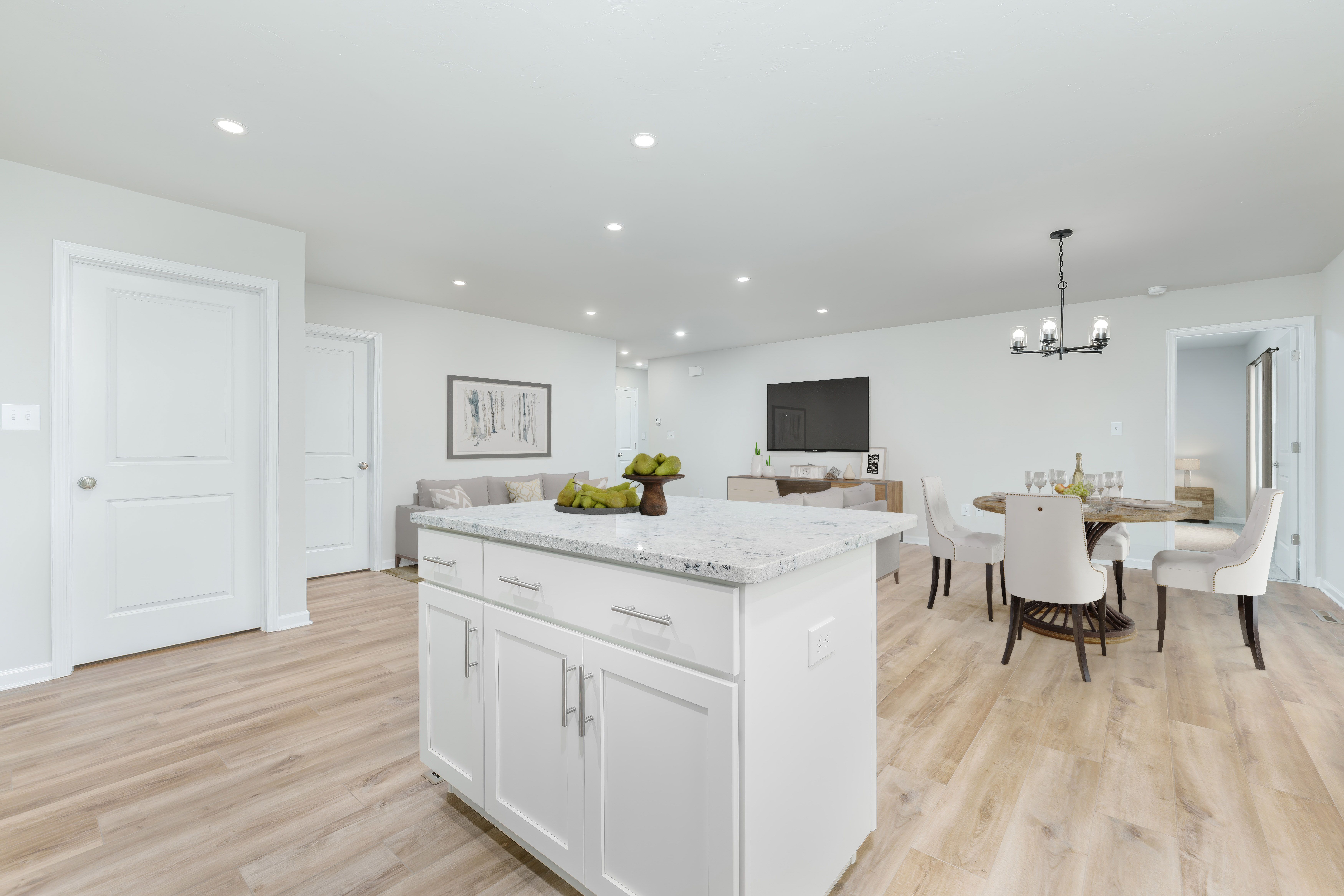 Large island overlooking open living and dining area with luxury vinyl plank flooring and recessed lighting.