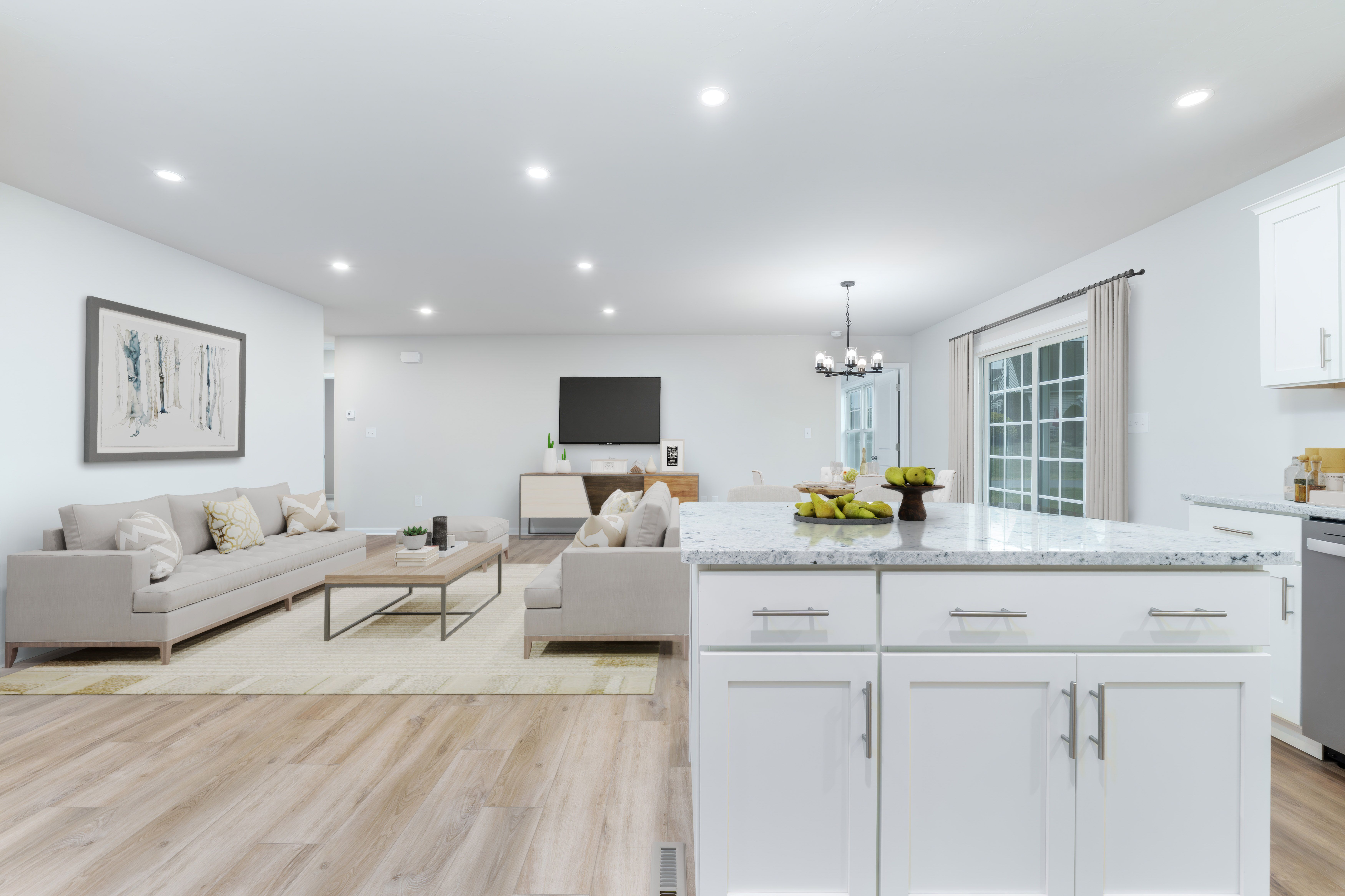 View from kitchen island toward living room with sofas, coffee table, dining area, and sliding glass door.