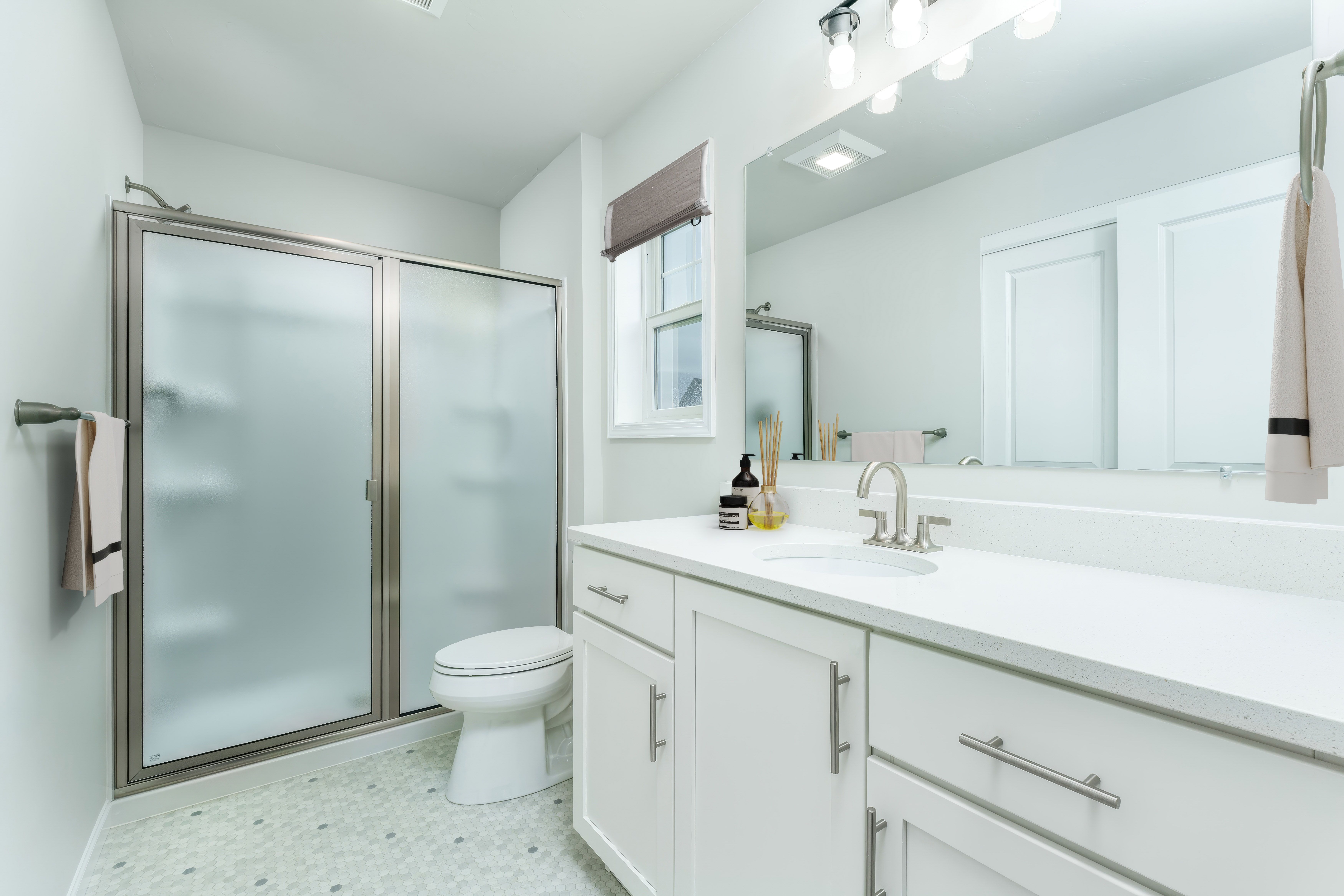 Owners bathroom with glass shower enclosure, double vanity, large mirror, and light tile flooring.