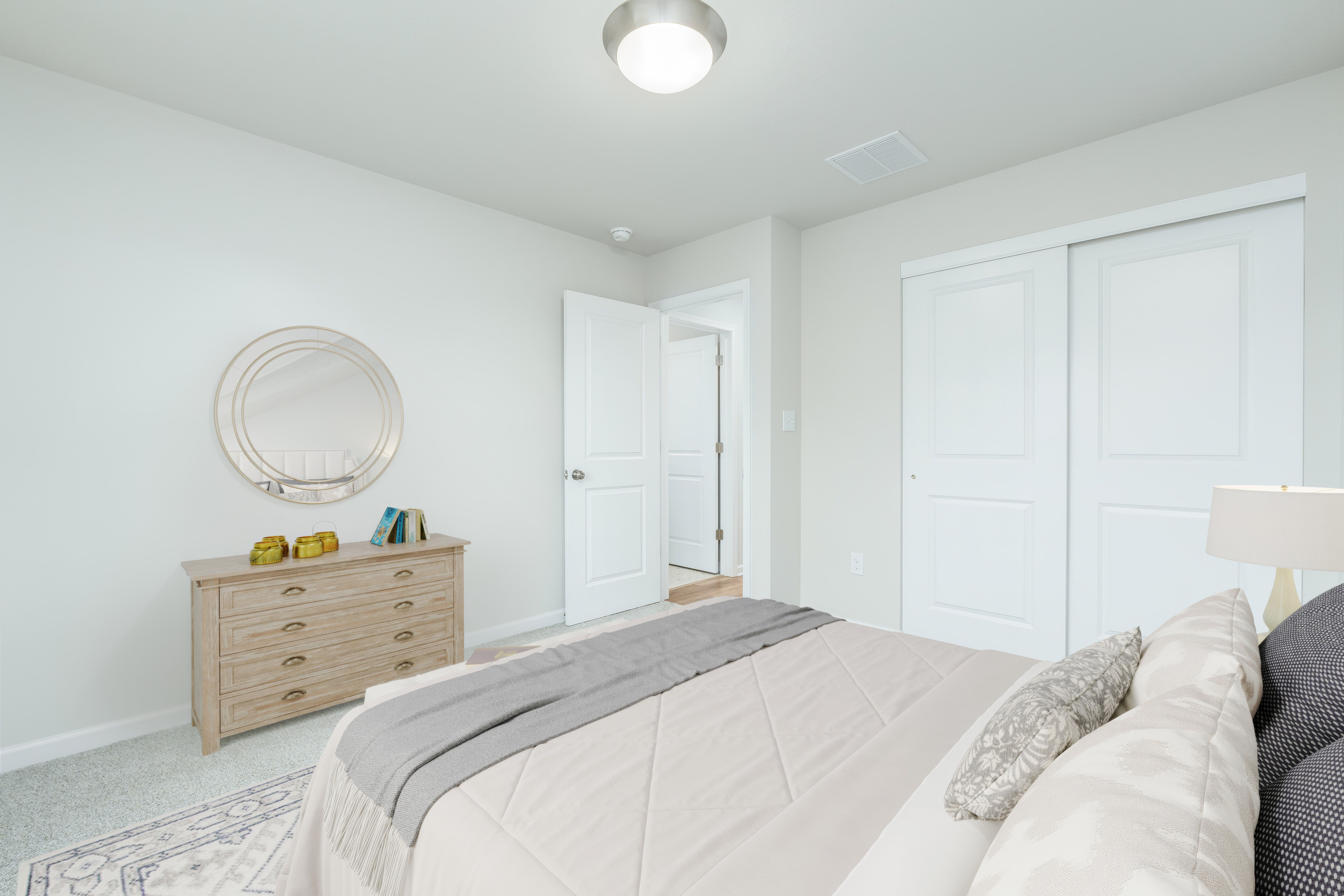 Bedroom with neutral bedding, dresser with round mirror, double closet doors, and soft carpet flooring.