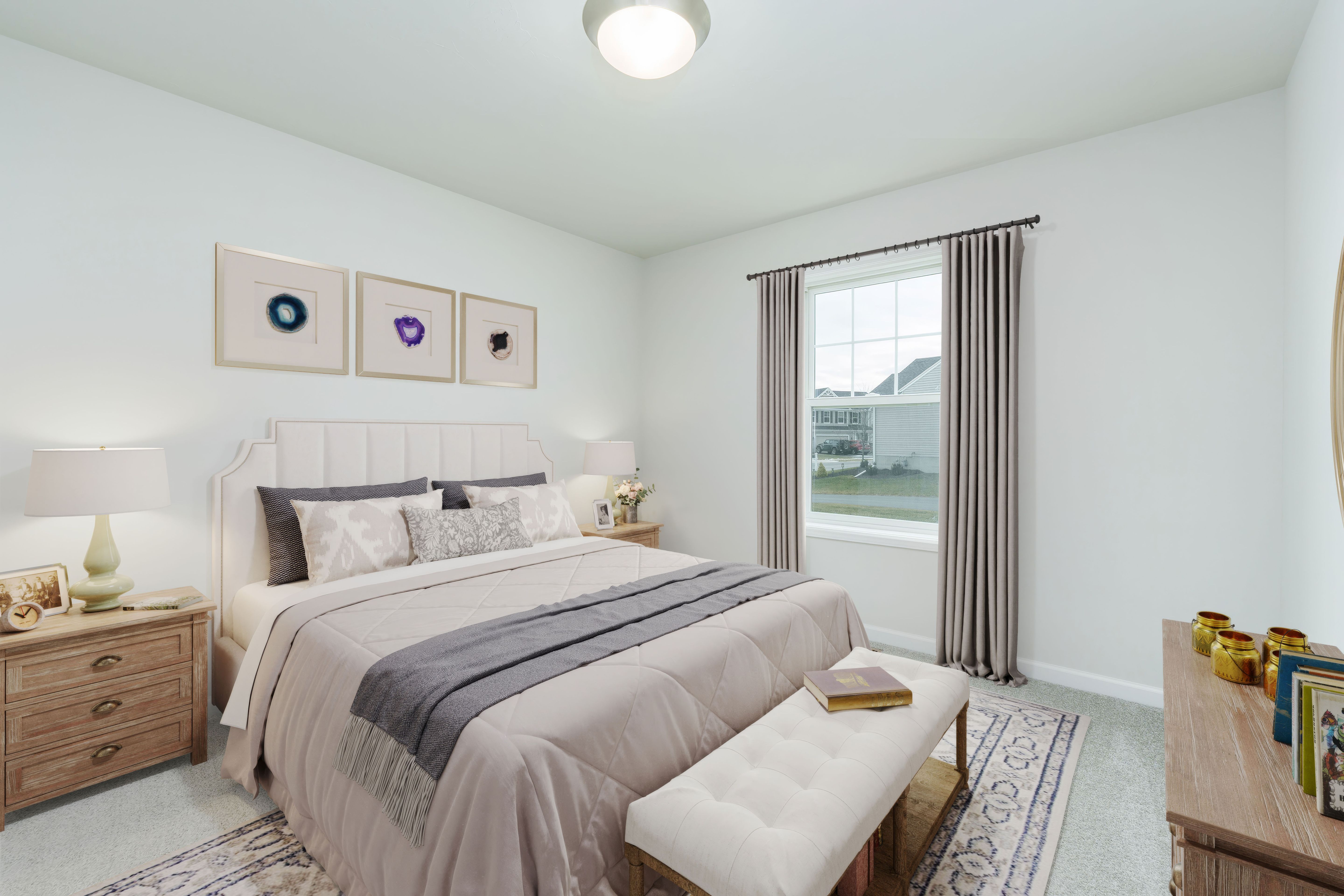 Cozy bedroom with upholstered bed, layered bedding, bedside tables, area rug, and window with long curtains.