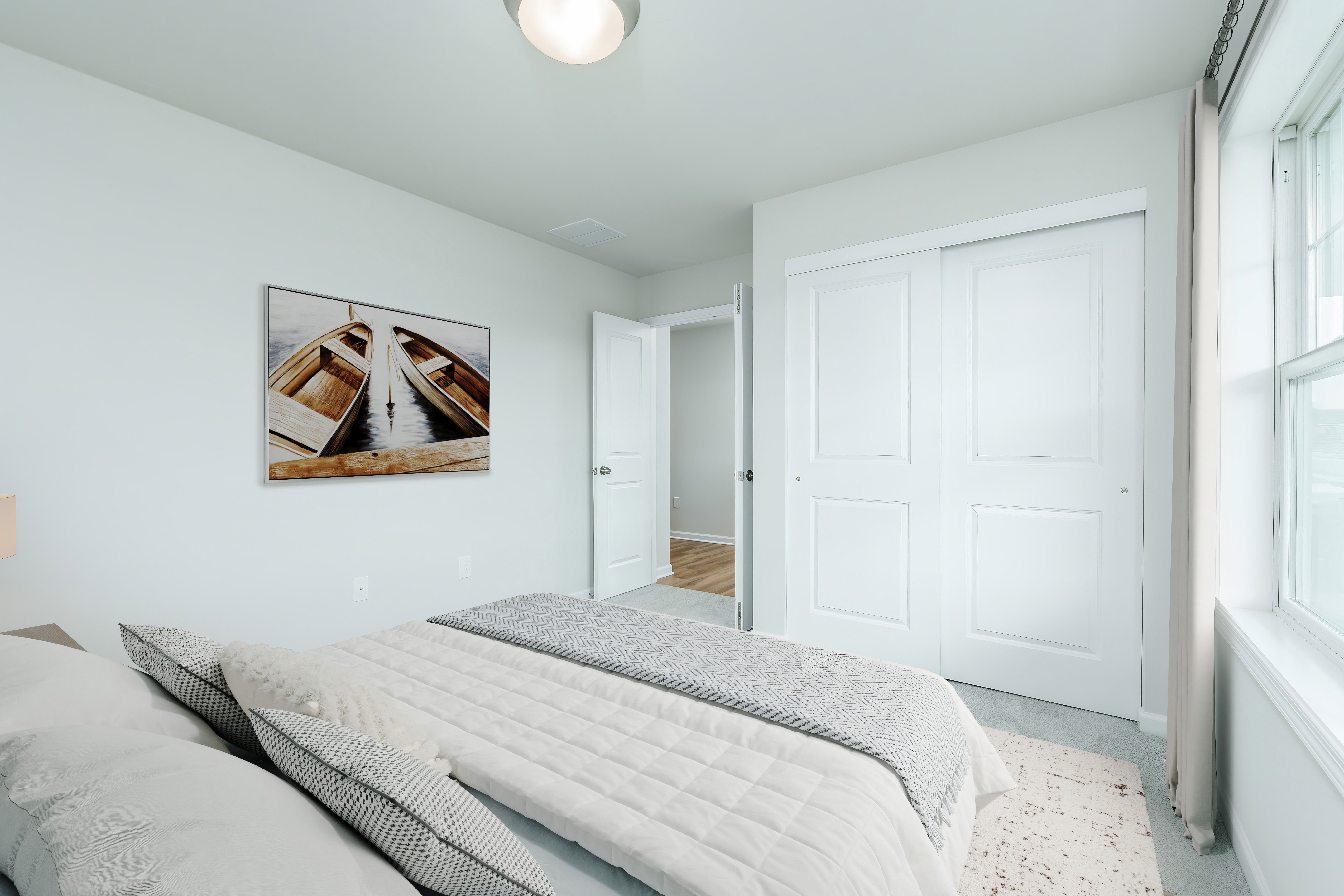 Bedroom with neutral bedding, large window with curtains, twin nightstands, and soft carpet flooring.