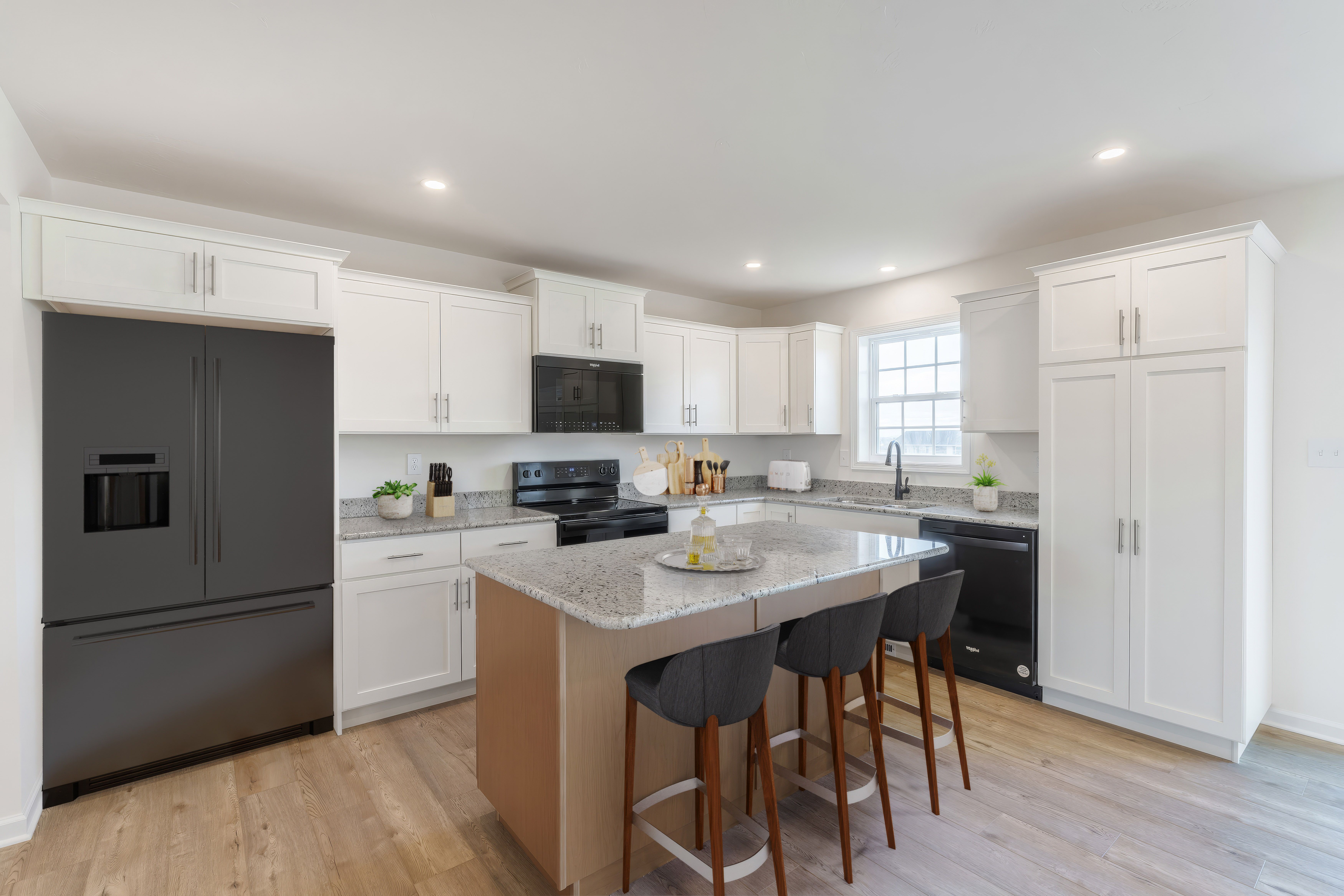 Modern kitchen with large island seating, black appliances, and luxury vinyl plank flooring