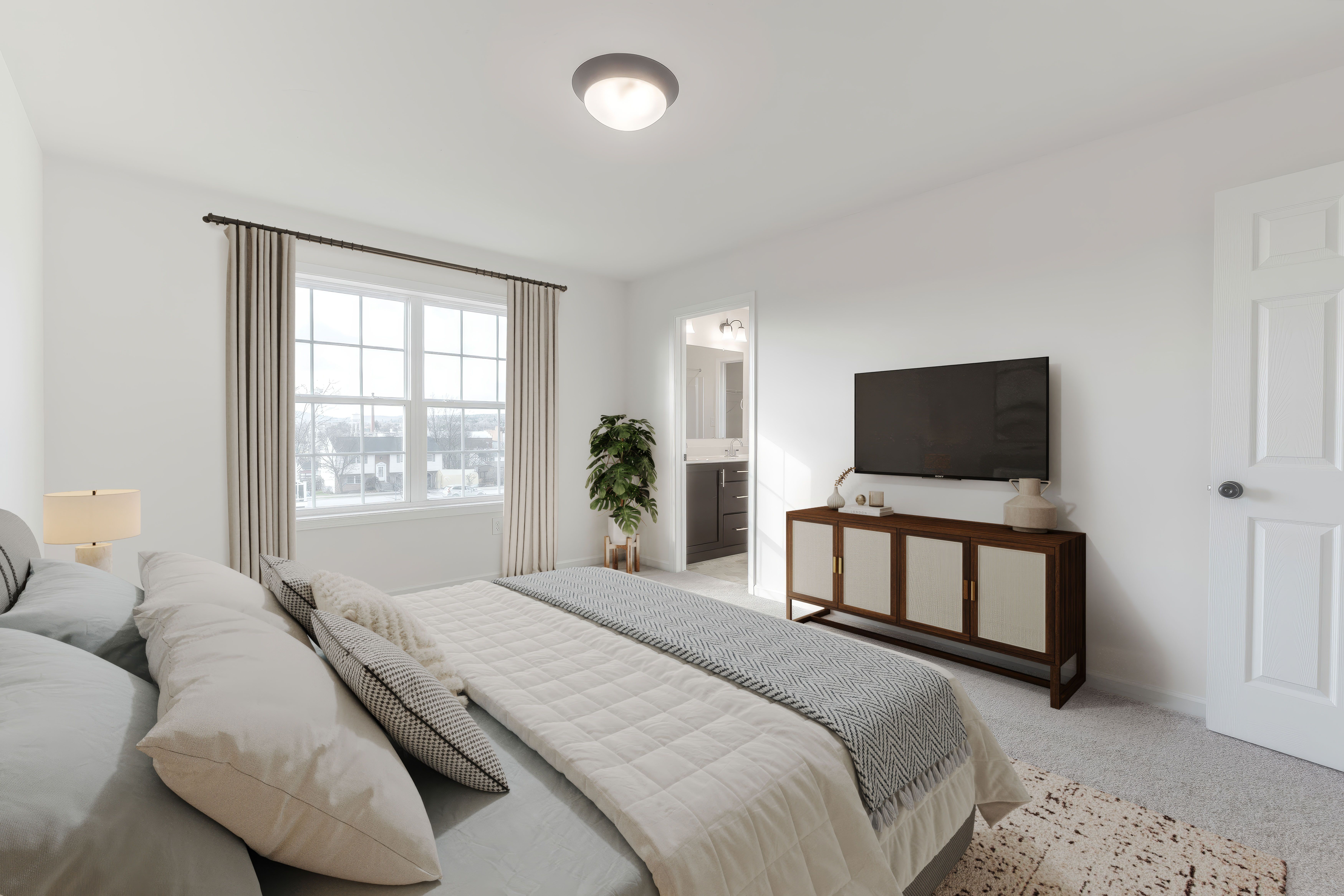 Owners bedroom with mounted TV, dresser, and open doorway to private bathroom