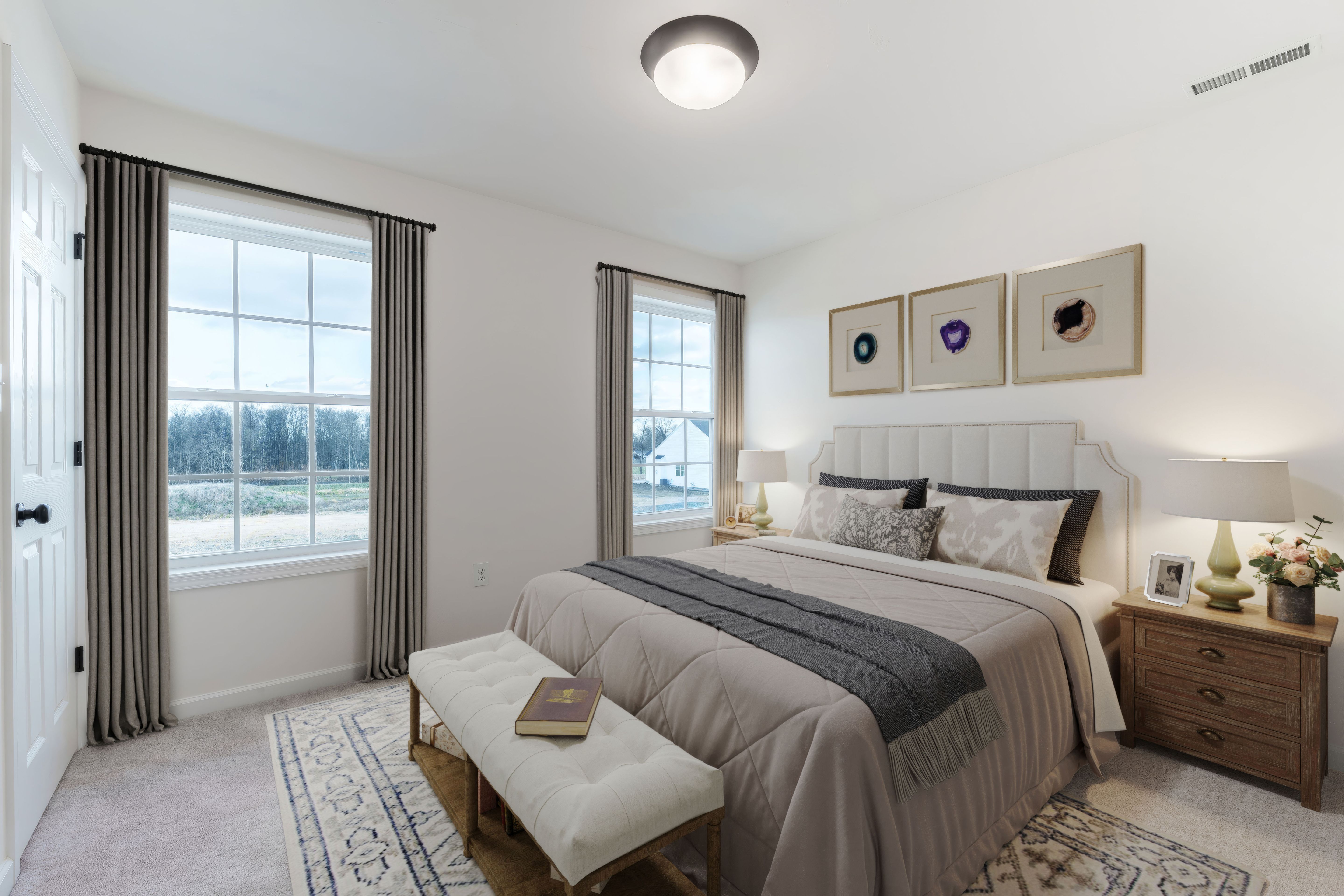Light-filled bedroom with upholstered bed, bench seating, and dual windows with serene outdoor views