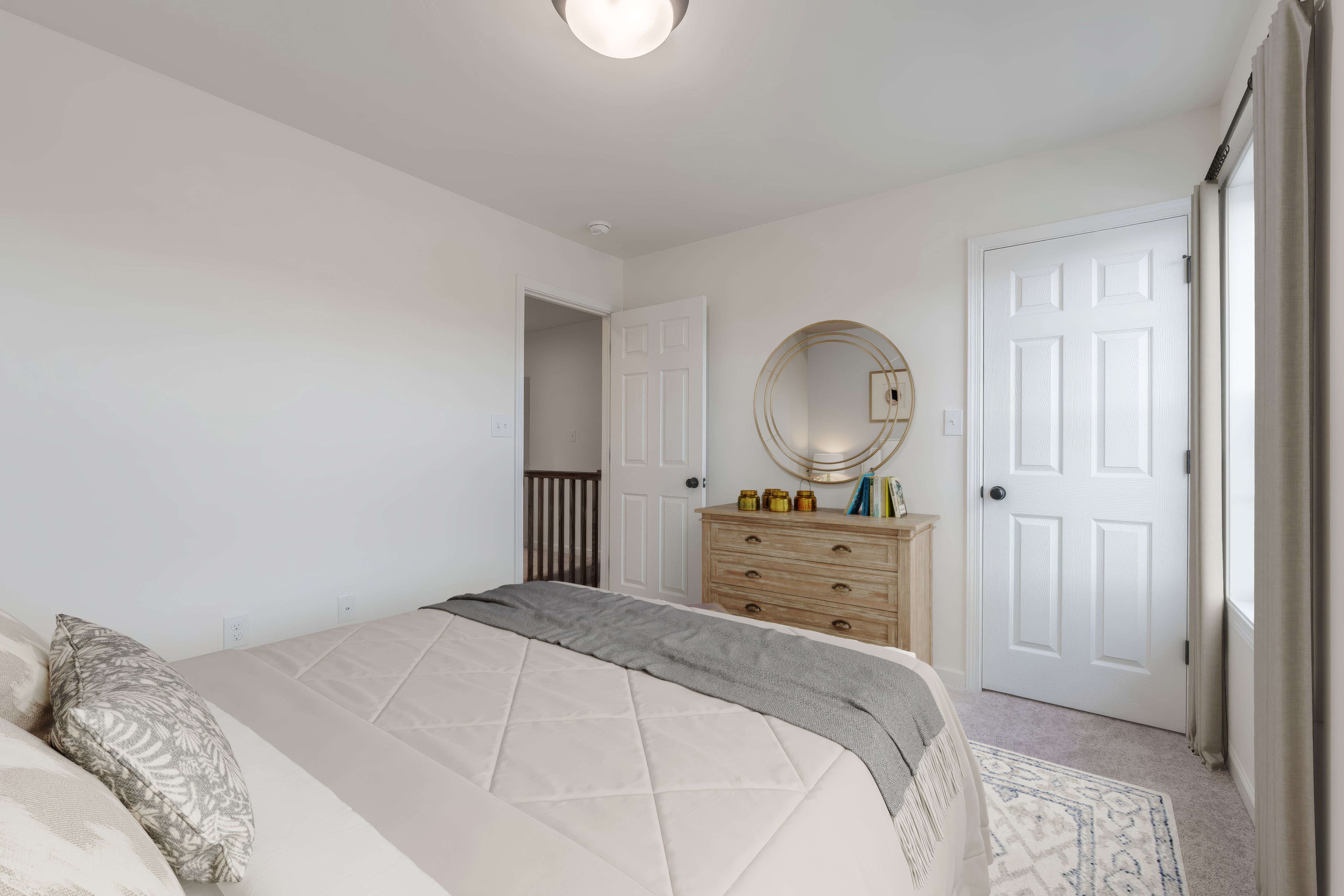 Bedroom with dresser, round mirror, open door, and soft carpet in warm neutral palette