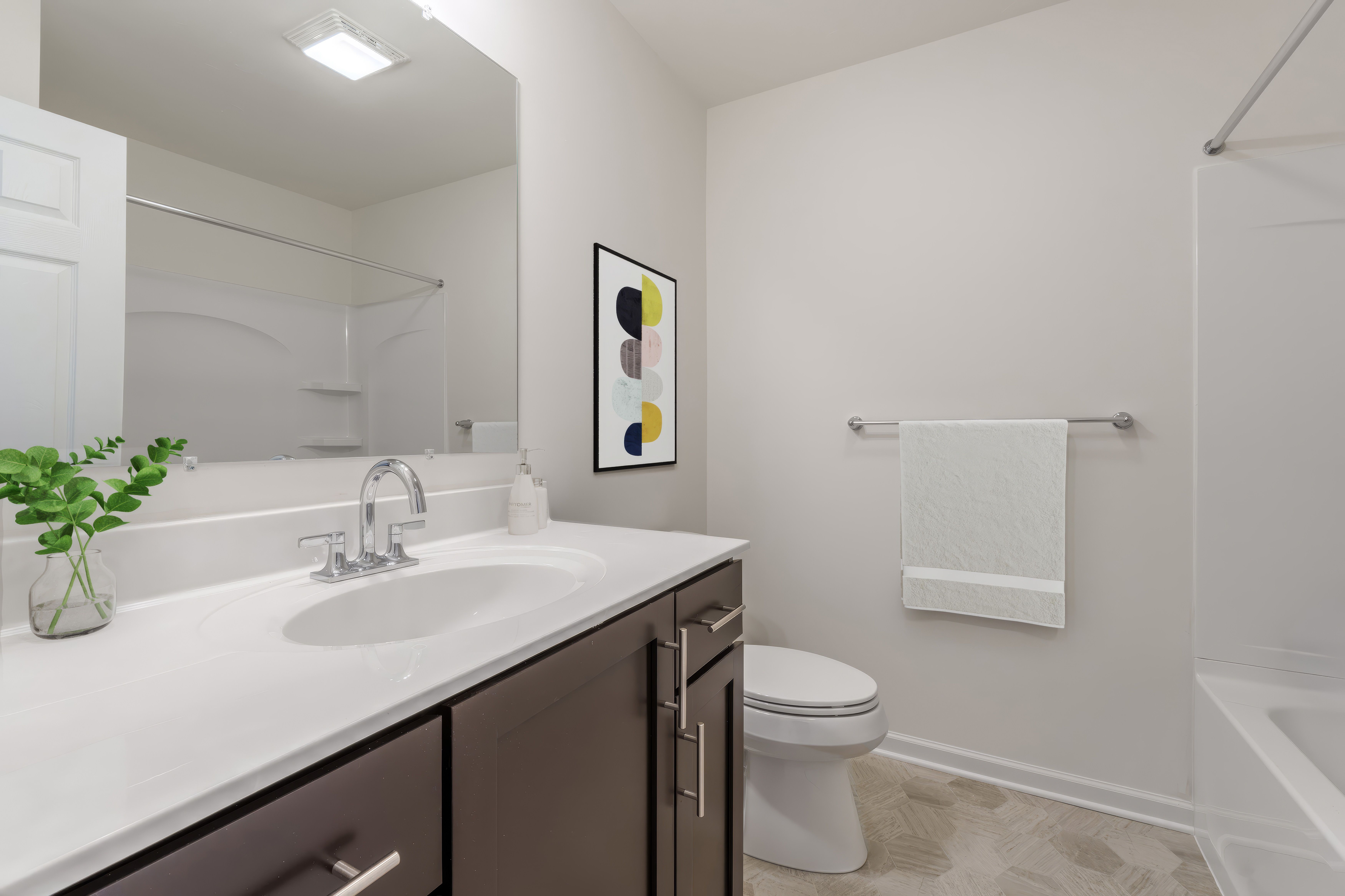 Bright bathroom with white vanity, chrome faucet, large mirror, and tub shower with neutral finishes