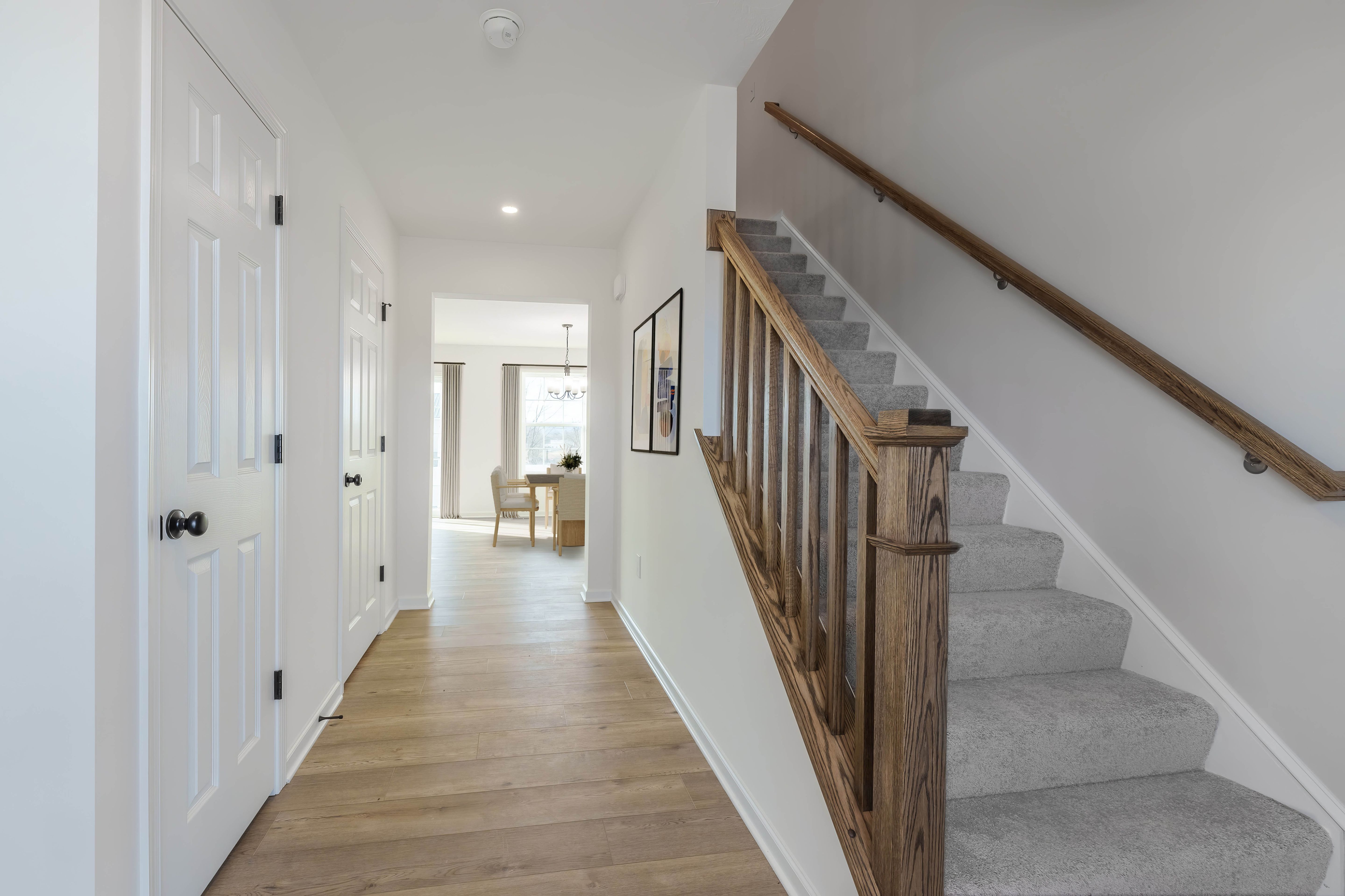 Bright foyer with vinyl plank flooring, carpeted staircase with wood railing, and view into dining area