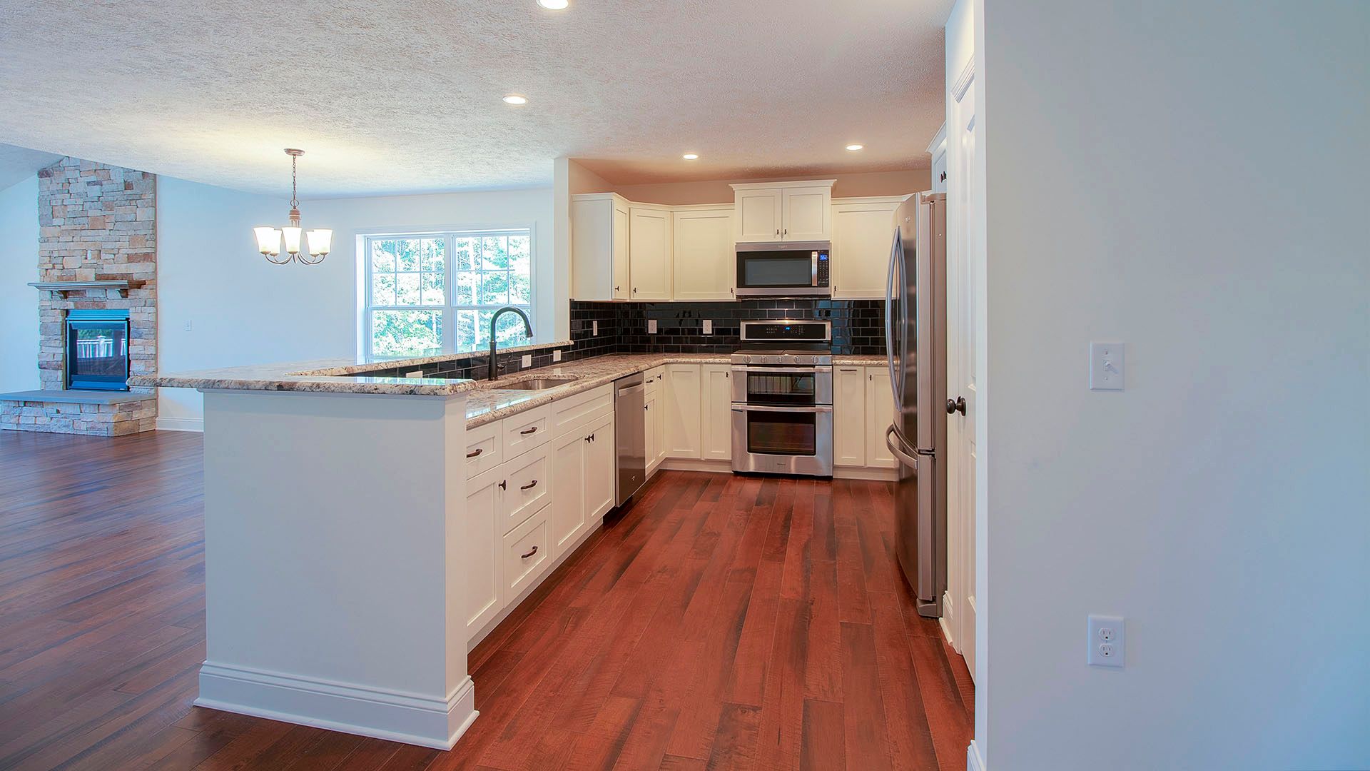 Kitchen with white cabinets and family room with stone fireplace, Aspen plan by S&A Homes