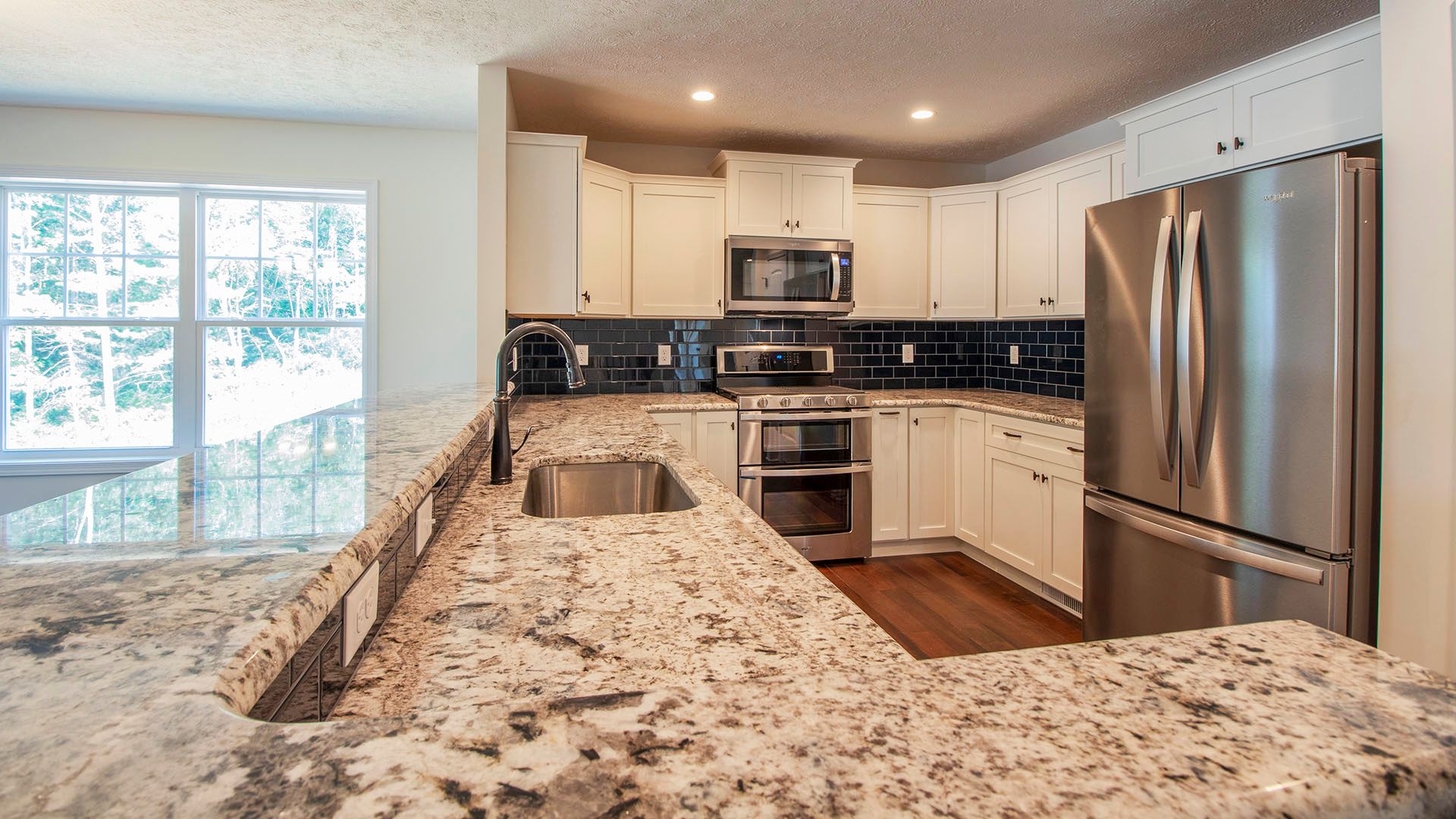 Kitchen with u shaped granite countertops and bar overhang, stainless appliances, and dark backsplash