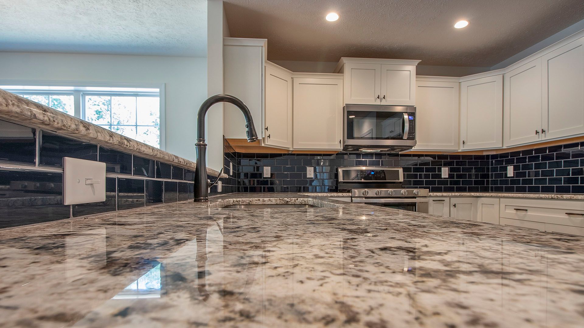 Granite kitchen countetops with stainless steel undermount sink, white cabinets, stainless appliances and dark backsplash