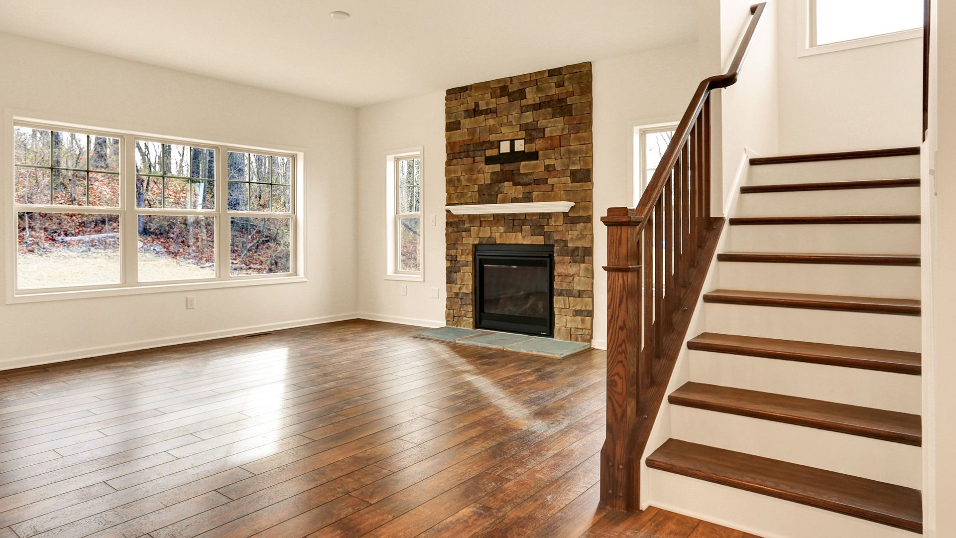 Family room with hardwood flooring, stone fireplace and oak stairs with white treads, Fairmont plan by S&A Homes