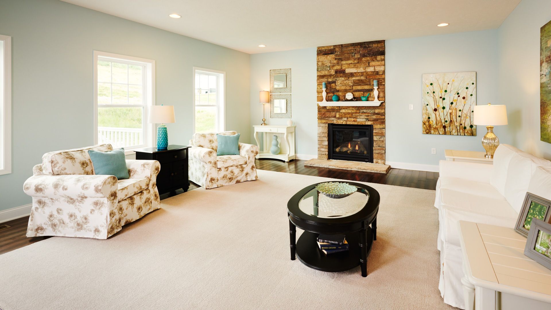 Furnished family room with floor rug, three windows and gas fireplace with stone surround