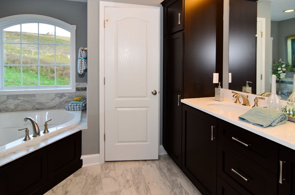 Owner's bath with corner tub with window above, dark vanity cabinets, and ceramic tile floor
