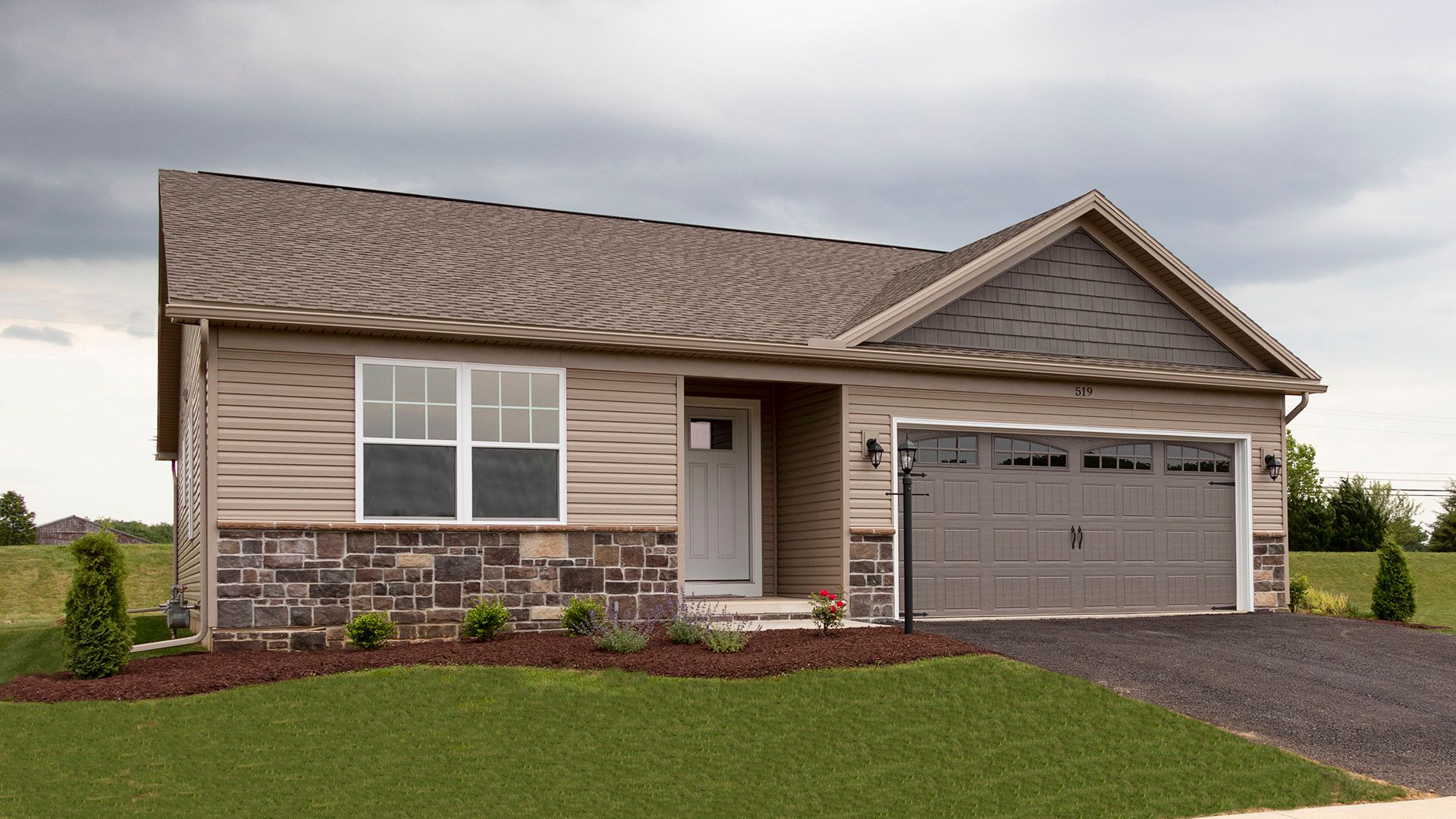 Exterior front view of the Elmcrest A ranch floorplan by S&A Homes - single storyhome with vinyl siding, stone kneewall, and two car garage with gable above