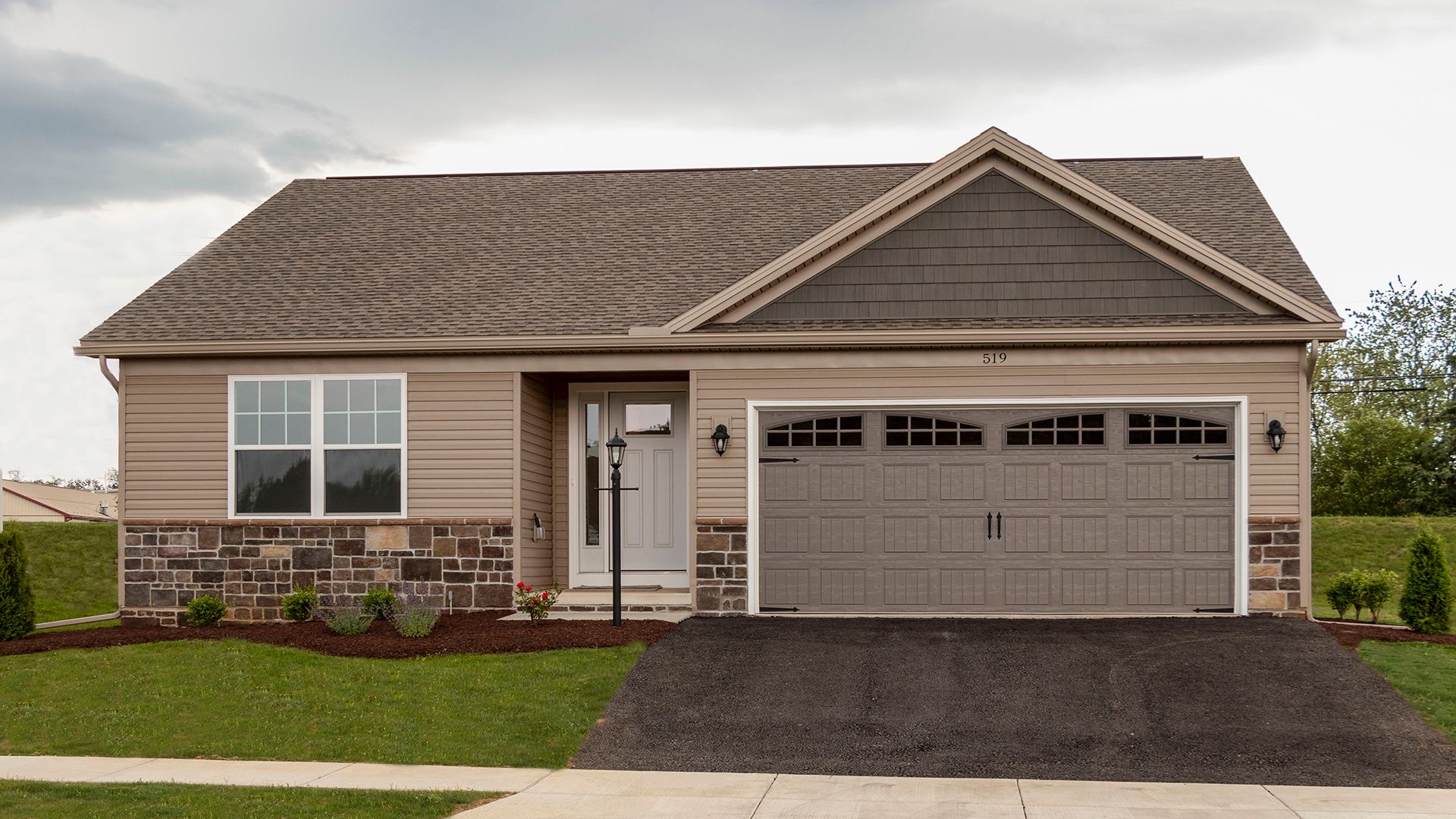 Exterior front view of the Elmcrest A ranch floorplan by S&A Homes - single storyhome with vinyl siding, stone kneewall, and two car garage with gable above