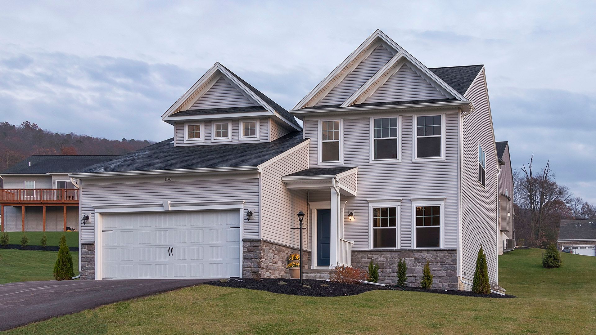 Front exterior of Crestmont B floorplan by S&A Homes - two story home with vinyl siding, partial stone kneewall, and dormer above two car garage