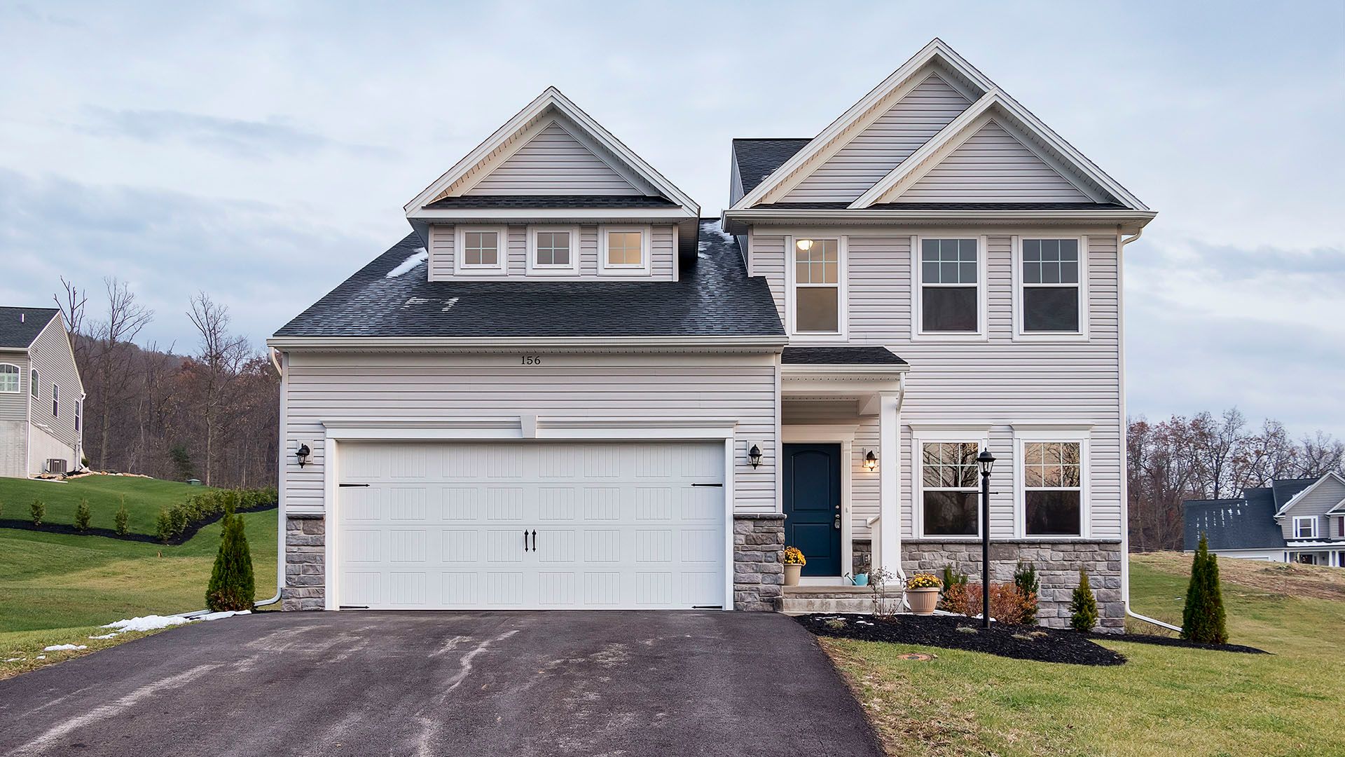 Front exterior of Crestmont B floorplan by S&A Homes - two story home with vinyl siding, partial stone kneewall, and dormer above two car garage