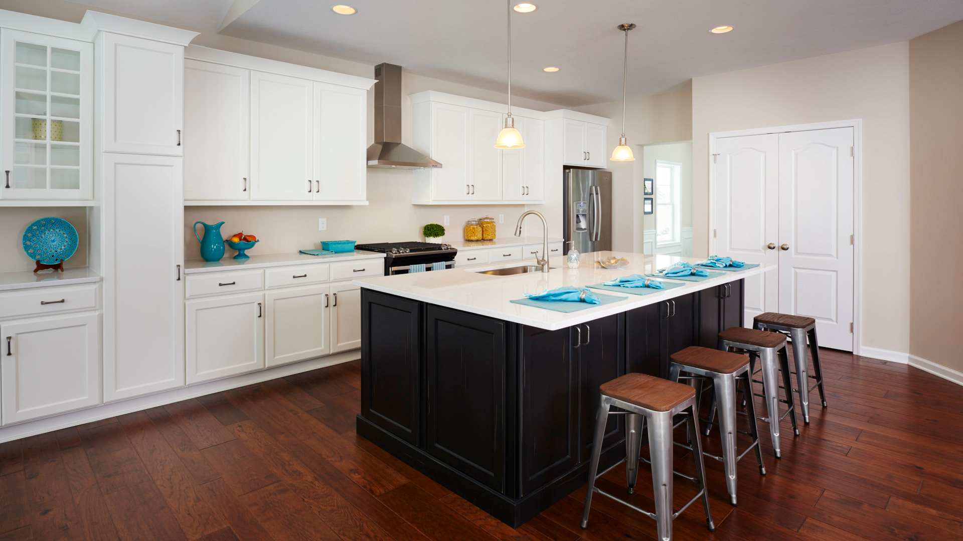 Kitchen with white cabinetry, large center island with dark base cabinets and stools at bar overhang, and hardwood flooring