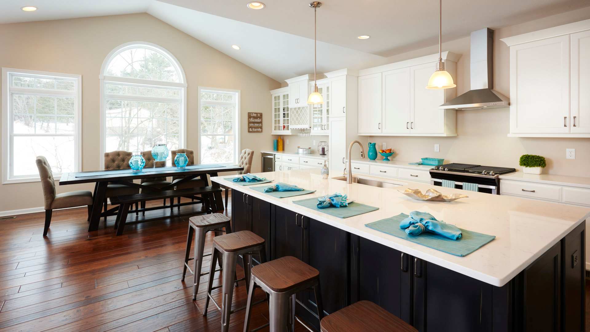 Kitchen and keeping room areas in the Dartmouth floorplan - white cabinetry, quartz countertops, and wall of windows.