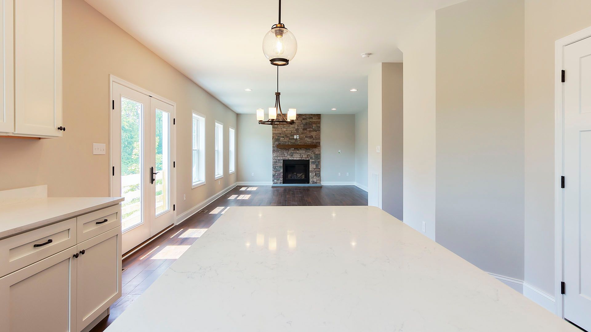 Kitchen area looking into great room, quartz island, hardwood flooring, stone fireplace