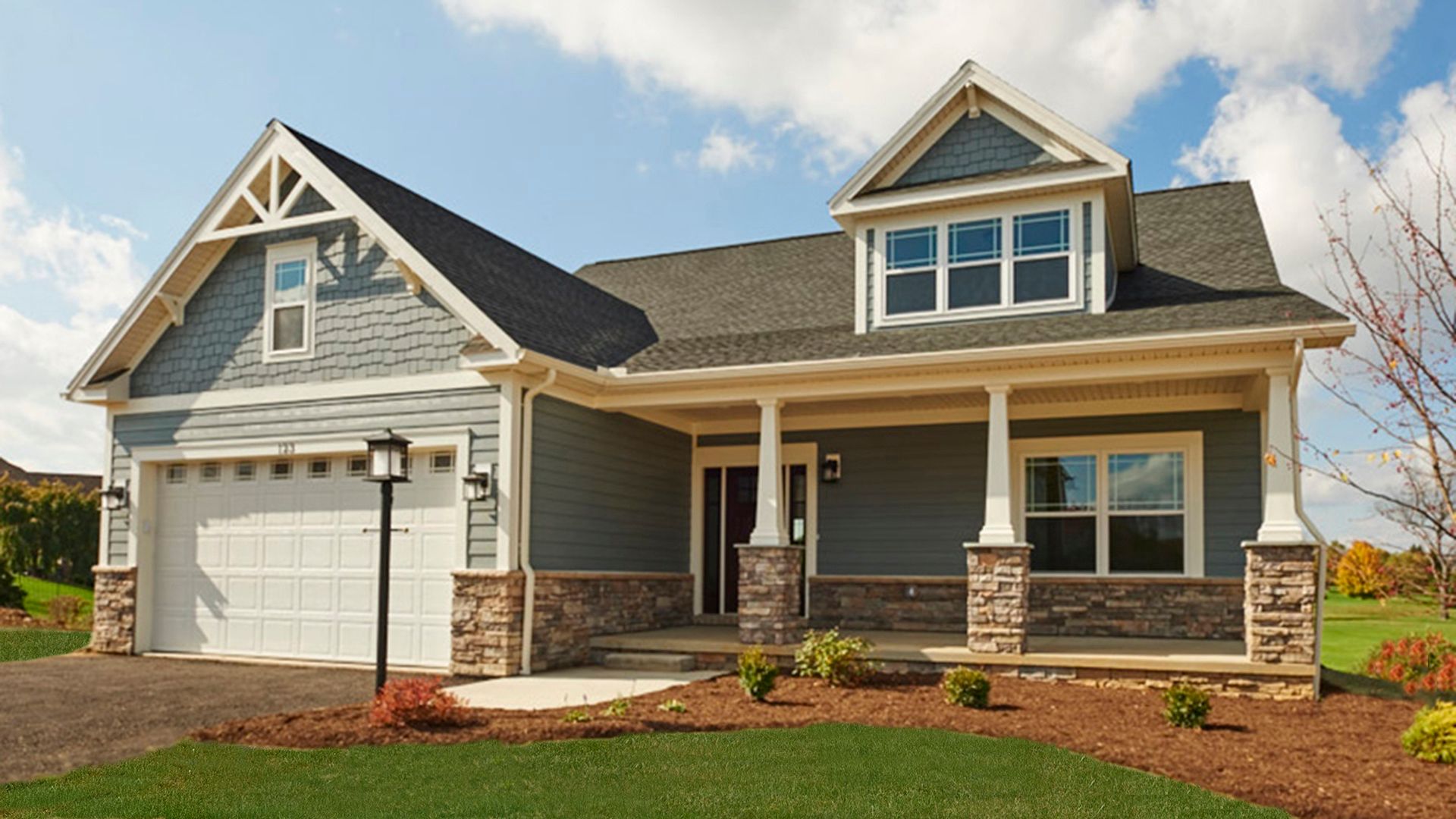 Exterior front view of the Chatham plan, available at Village at Canterbury in State College by S&A Homes - single level ranch plan with Craftsman style design, full front porch with dormer above, and partial stone front