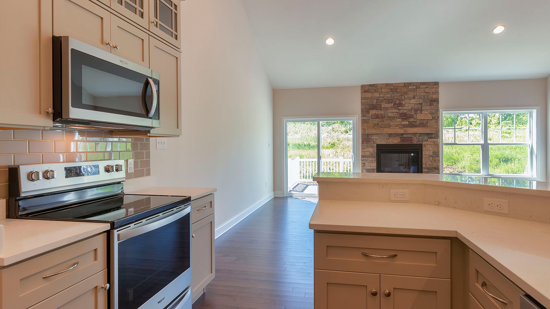 View from kitchen with stainless appliances into family room with stone fireplace