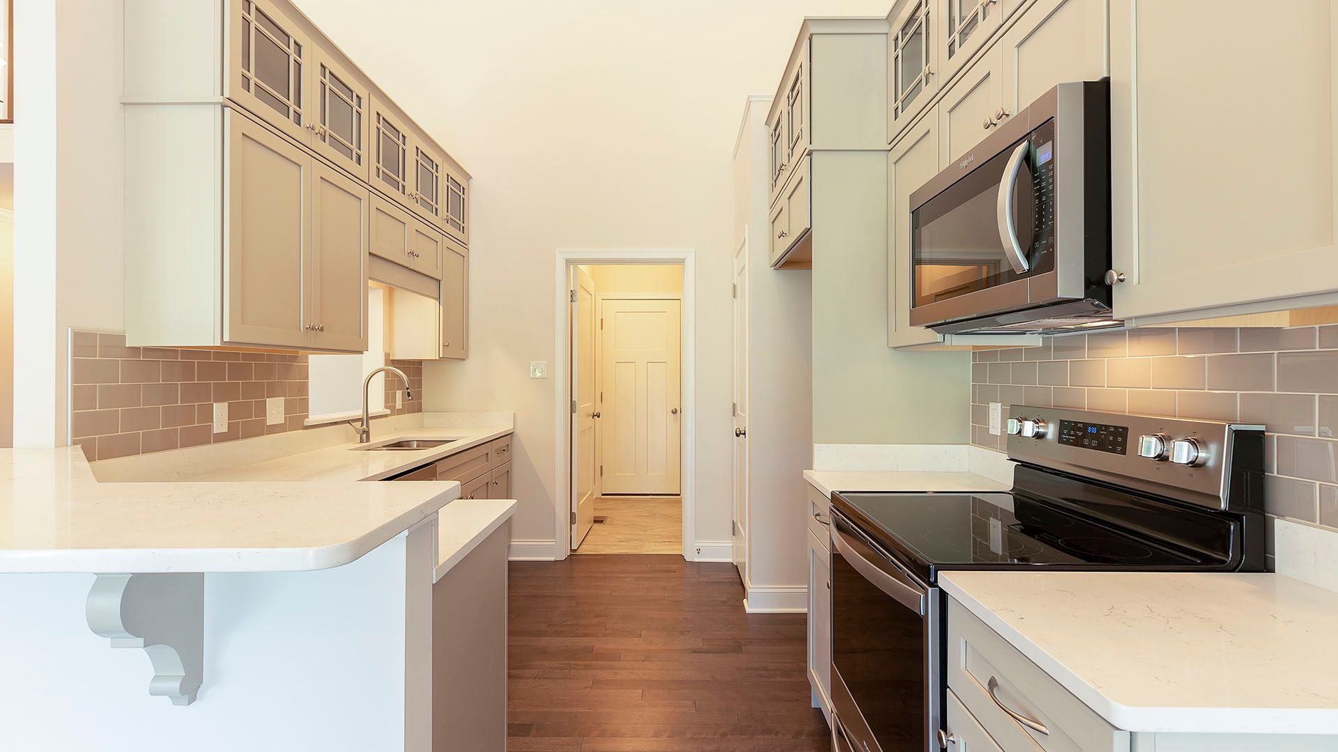 Kitchen with tan cabinets with glass, quartz countertops, stainless appliances and hardwood flooring