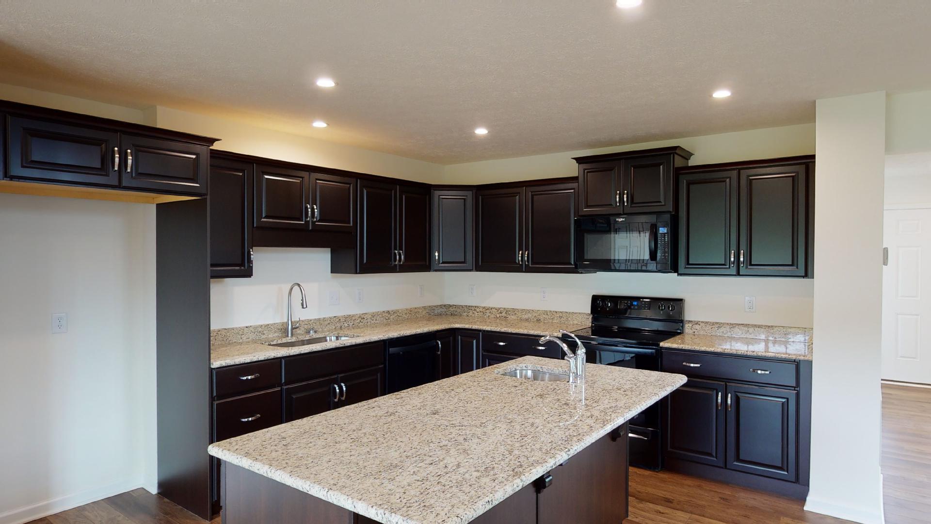 Kitchen with dark cabinetry, center island, granite countertops and black appliances.