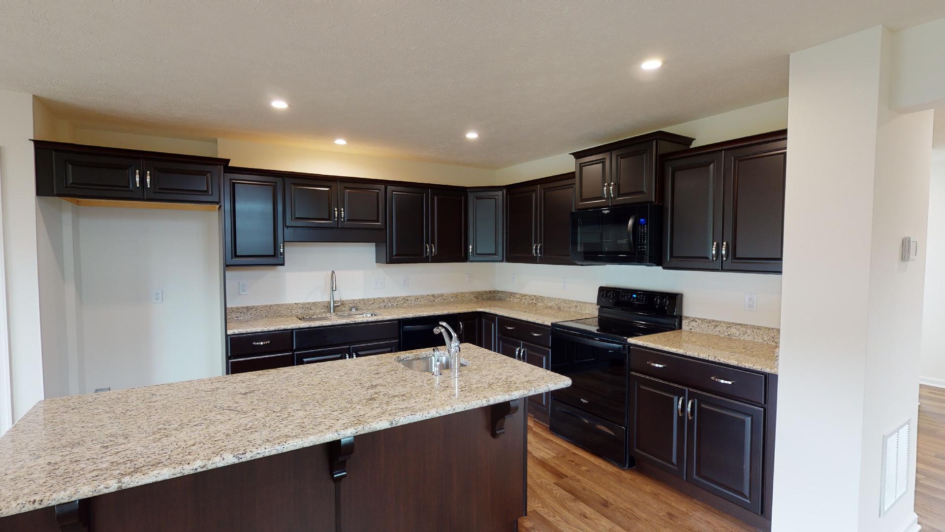 Kitchen with dark cabinetry, center island, granite countertops and black appliances.