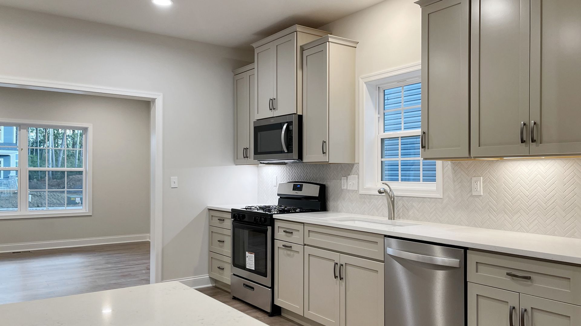 Kitchen with off white cabinets, window above sink, stainless steel appliances, white quartz countertops, and hardwood flooring - facing doorway to dining room